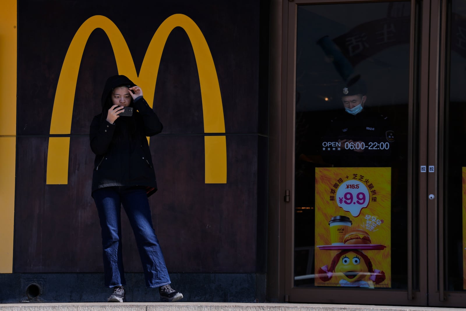 A woman looks at her phone near a McDonald's fast food restaurant along the popular Wangfujing shopping street in Beijing, China, Thursday, March 6, 2025. (AP Photo/Ng Han Guan)