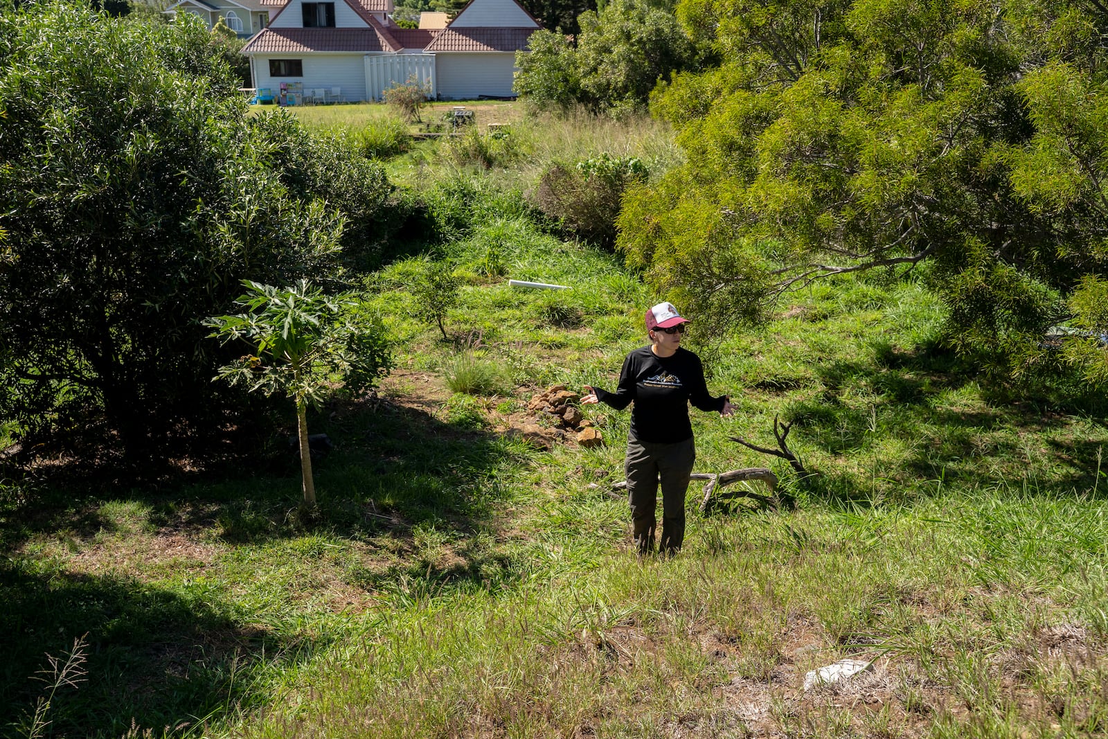 Harriet Parsons, a firewise community support specialist for the Hawaii Wildfire Management Organization, points to the drylands behind a house in her community, Tuesday, Feb. 25, 2025, in Kamuela, Hawaii. (AP Photo/Mengshin Lin)