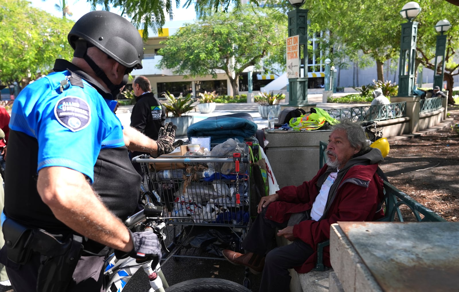 Omar Gonzalez, 70, who is homeless, right, talks with a security guard he sits on a park bench with his belongings as temperatures are forecast to be in the forties this evening Wednesday, Jan. 8, 2025, in Miami. (AP Photo/Lynne Sladky)