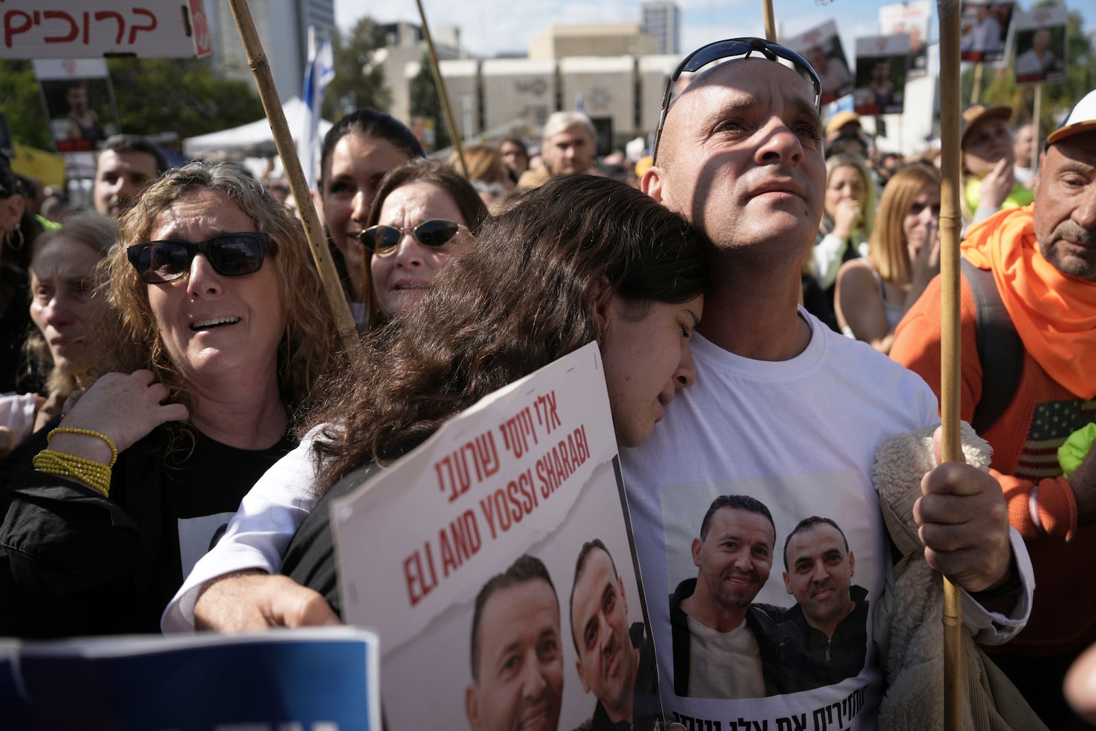 People holding posters with photos of Israelis hostages Eli Sharabi, Or Levy and Ohad Ben Ami, react at the so-called "hostages square" as they watch their release live on a television screen in Tel Aviv, Israel on Saturday, Feb. 8, 2025. (AP Photo/Oded Balilty)