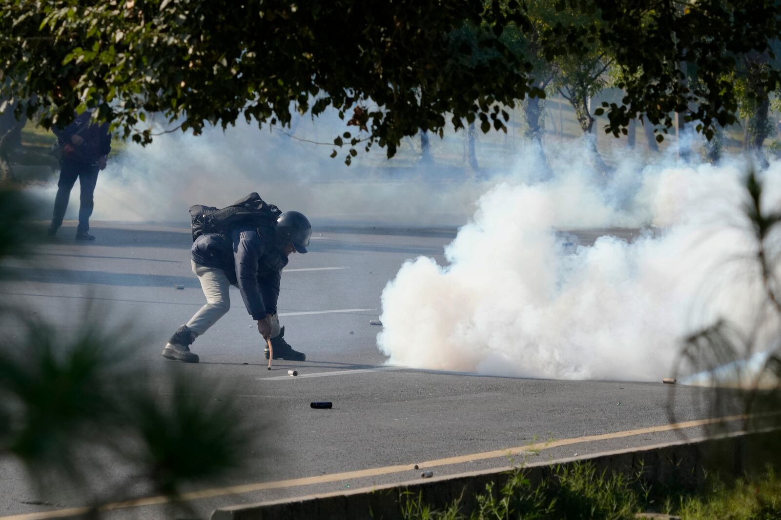 A police officer removes a tear gas shell thrown back by supporters of imprisoned former premier Imran Khan's Pakistan Tehreek-e-Insaf party, during clashes, in Islamabad, Pakistan, Tuesday, Nov. 26, 2024. (AP Photo/Anjum Naveed)