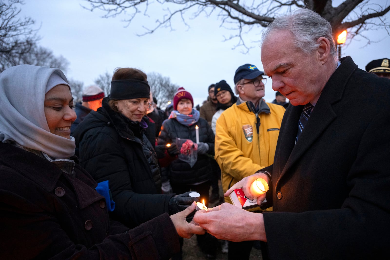 Sen. Tim Kaine, D-Va., right, lights candle at the start of a candlelight vigil, Wednesday, Feb. 5, 2025 in Alexandria, Va., for the victims of the mid-air collision of an American Airlines jet and a Black Hawk helicopter at Reagan National Airport. (AP Photo/Kevin Wolf)