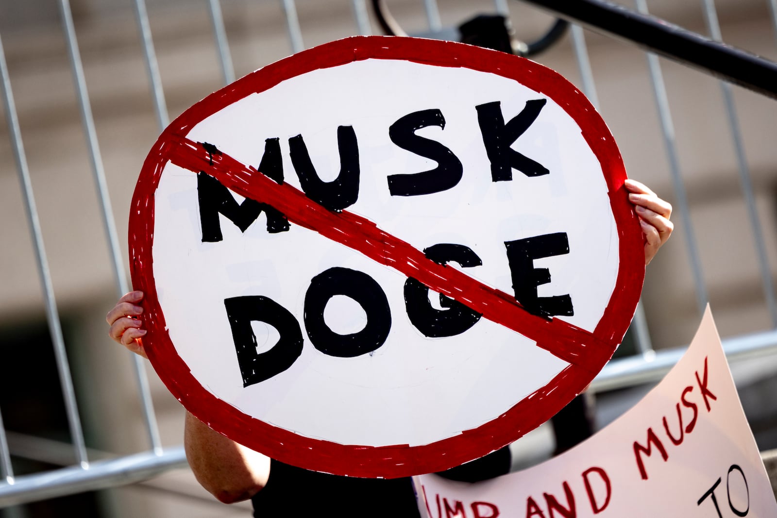 A demonstrator holds a poster displaying a prohibited traffic sign reading "Musk DOGE" during a rally to protest President Trump's policies on Presidents Day Monday, Feb. 17, 2025, in Los Angeles. (AP Photo/Etienne Laurent)