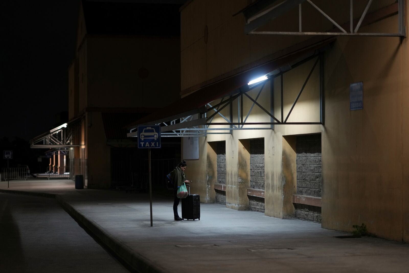 A woman waits for a bus at a station in San Pedro Sula, Honduras, Tuesday, Dec. 3, 2024. (AP Photo/Moises Castillo)