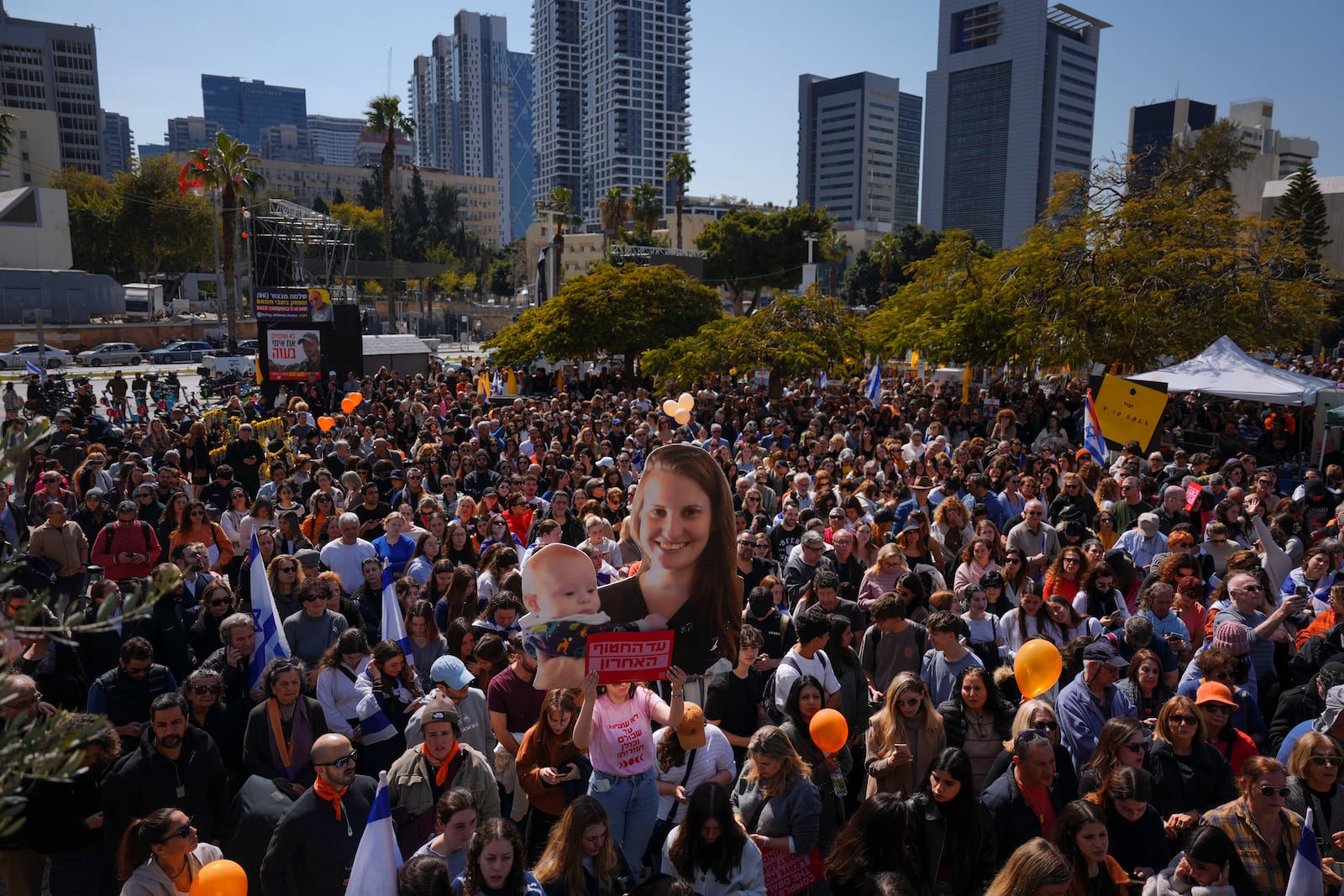 People watch a live broadcast from the funeral of slain hostages Shiri Bibas and her two children, Ariel and Kfir, at a plaza known as the Hostages Square in Tel Aviv, Israel, Wednesday, Feb. 26, 2025. The mother and her two children were abducted by Hamas on Oct. 7, 2023, and their remains were returned from Gaza to Israel last week as part of a ceasefire agreement with Hamas. (AP Photo/Ariel Schalit)