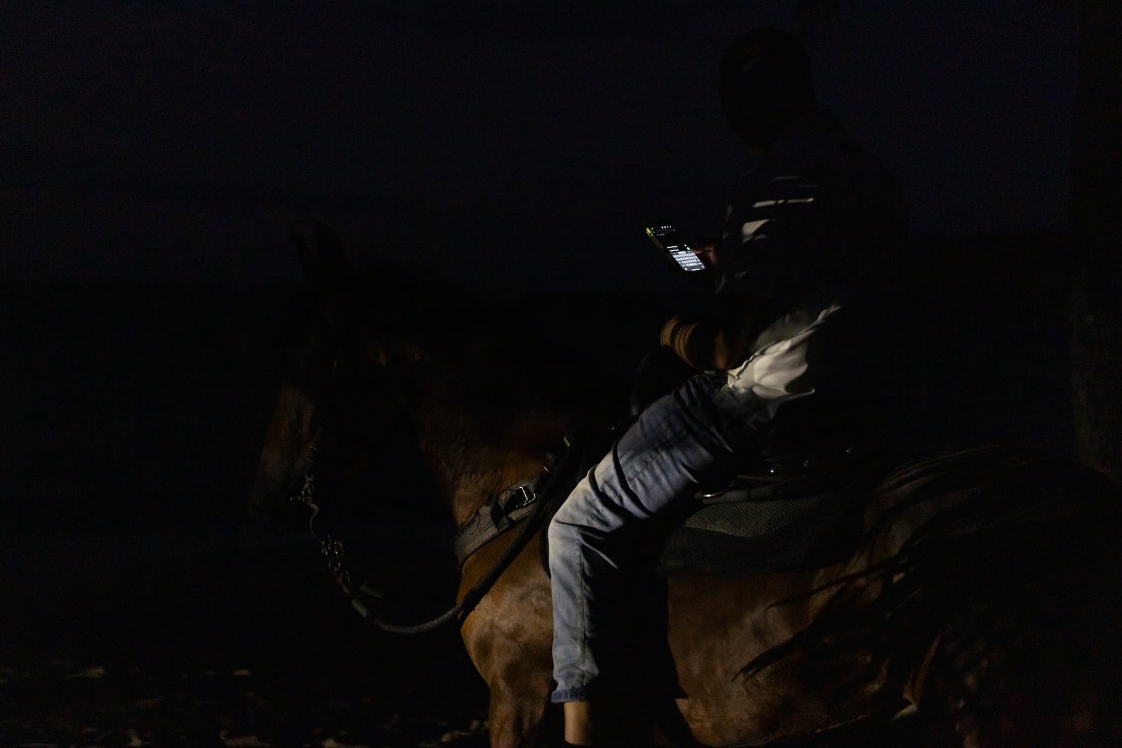 A horse rider uses a cell phone along a dark street during a blackout in Vega Alta, Puerto Rico, after sunset Tuesday, Dec. 31, 2024. (AP Photo/Alejandro Granadillo)