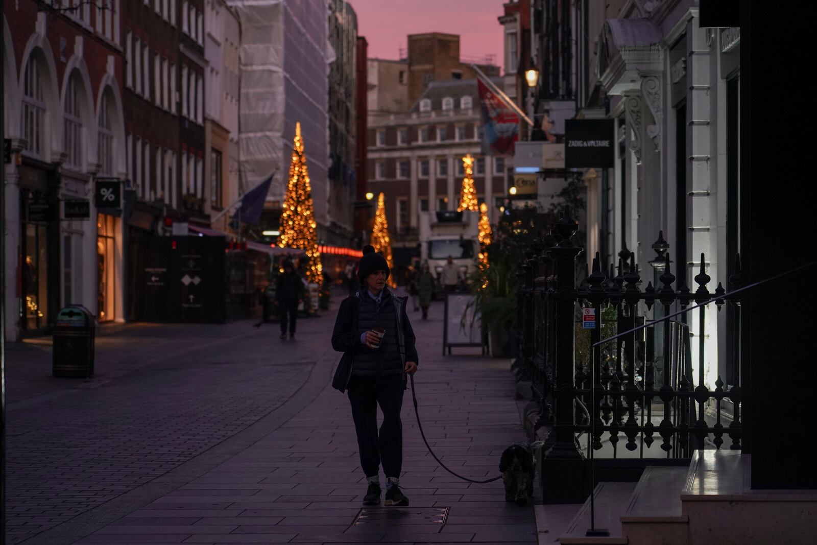 A woman walks a dog in a street of Mayfair at sunrise, in London, Friday, Nov. 29, 2024.(AP Photo/Alberto Pezzali)