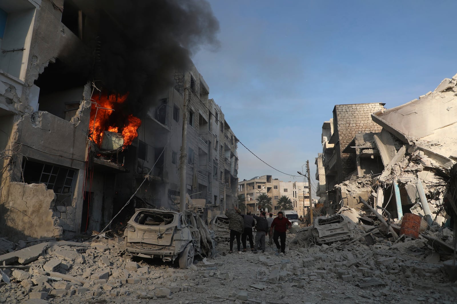 This photo provided by the Syrian Civil Defence White Helmets, which has been authenticated based on its contents and other AP reporting, shows Syrian residents gather near destroyed buildings, after Syrian government forces hit Idlib city, Syria, Monday, Dec. 2, 2024. (Syrian Civil Defence White Helmets via AP)