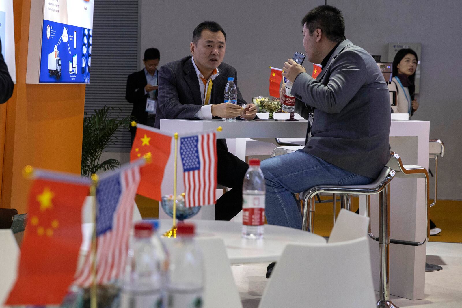 FILE - Visitors chat near American and Chinese flags displayed at a booth for an American company promoting environmental sensors during the China International Import Expo in Shanghai on Nov. 6, 2019. (AP Photo/Ng Han Guan, FIle)