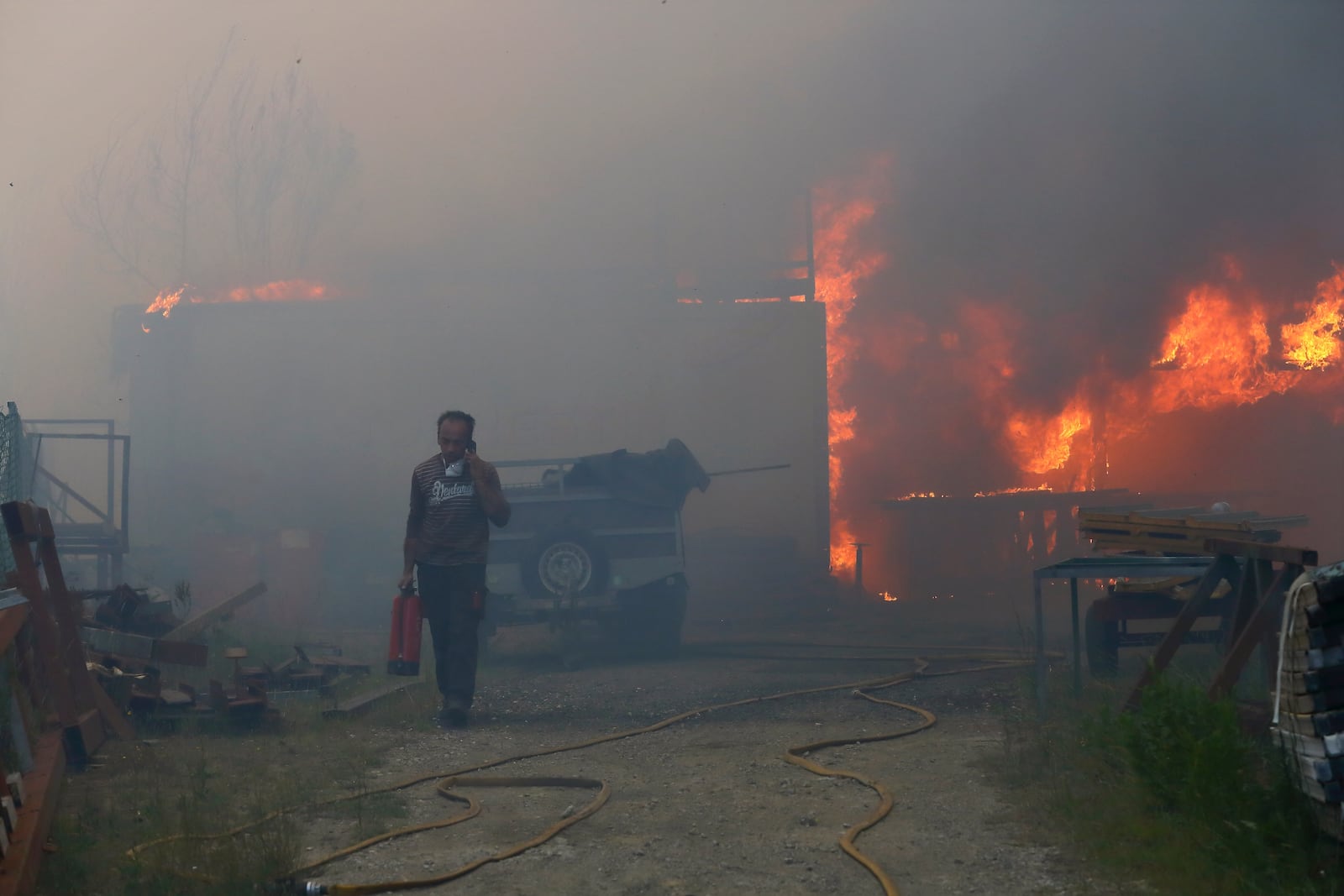 A man carries a fire extinguisher as he speaks on the phone while a metalworking warehouse burns in Sever do Vouga, a town in northern Portugal that has been surrounded by wildfires, Monday, Sept. 16, 2024. (AP Photo/Bruno Fonseca)