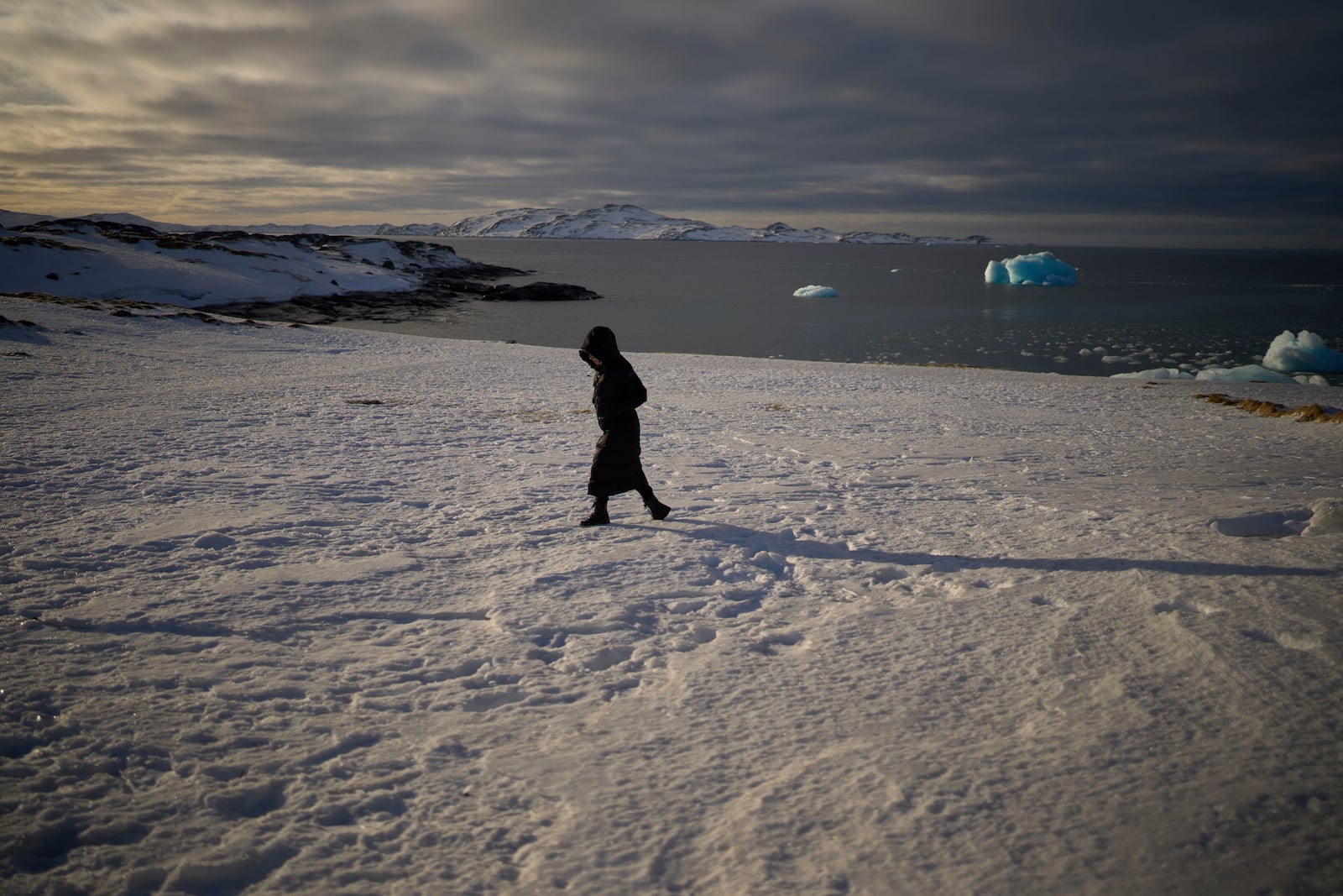 A woman walks along the shore of a beach while pieces of ice float in the sea of Nuuk, Greenland, Friday, Feb. 14, 2025. (AP Photo/Emilio Morenatti)