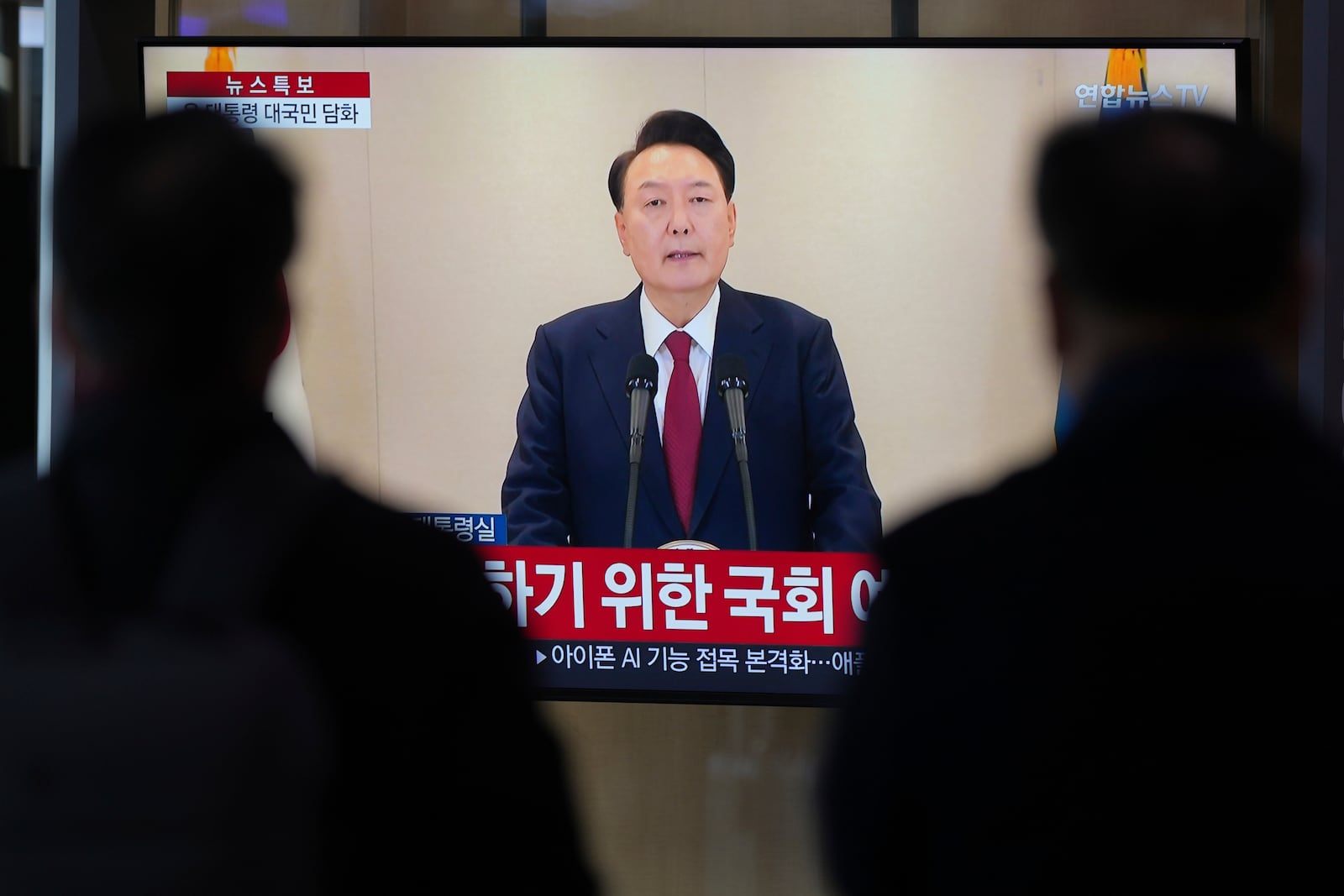 People watch a TV screen showing the live broadcast of South Korean President Yoon Suk Yeol's announcement at the Seoul Railway Station in Seoul, South Korea, Thursday, Dec. 12, 2024. (AP Photo//Lee Jin-man)