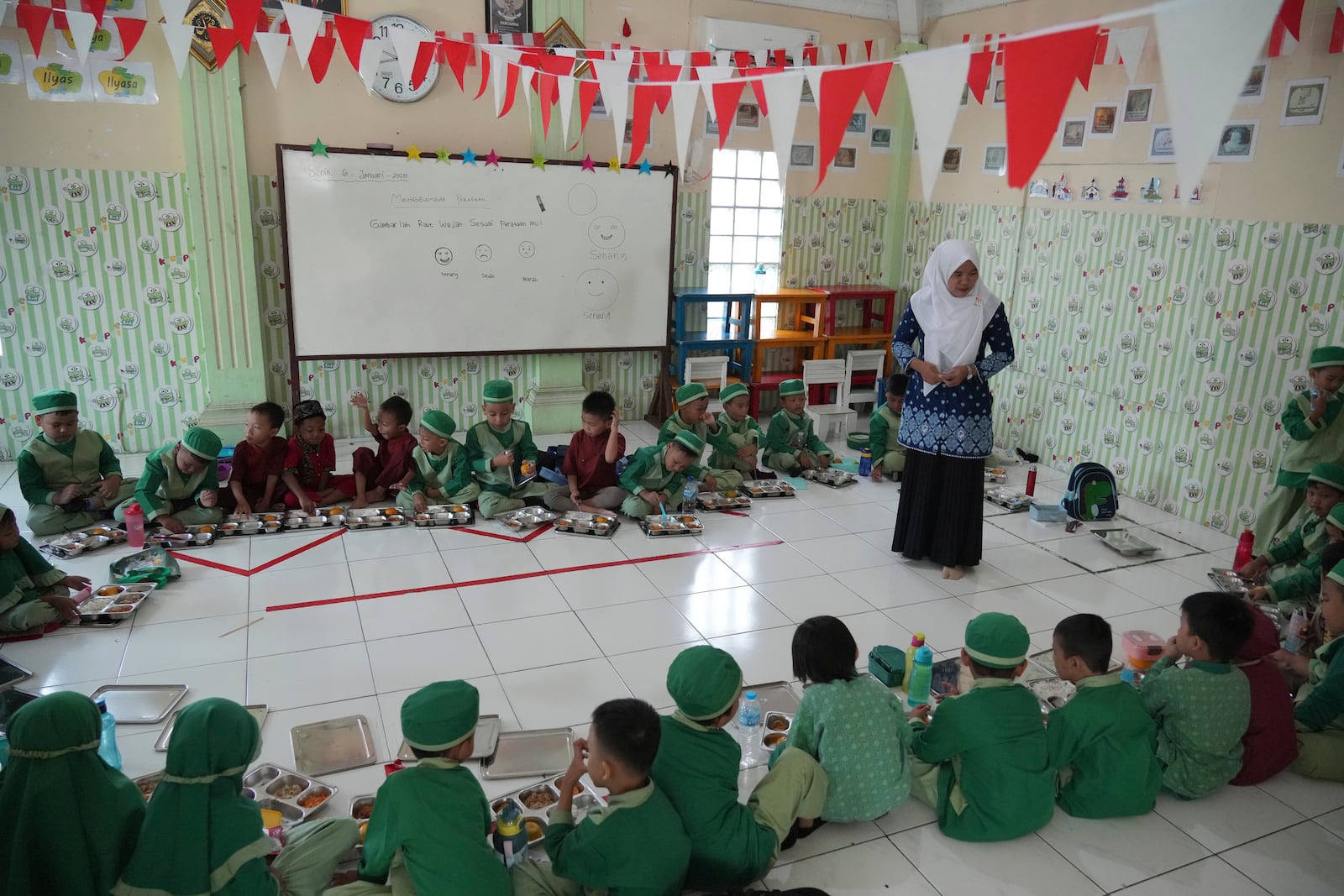 Students sit on the floor as they have their meals during the kick off of President Prabowo Subianto's ambitious free meal program to feed children and pregnant women nationwide despite critics saying that its required logistics could hurt Indonesia's state finances and economy at Early Childhood Education and Development in Jakarta, Indonesia, Monday, Jan. 6, 2025. (AP Photo/Achmad Ibrahim)