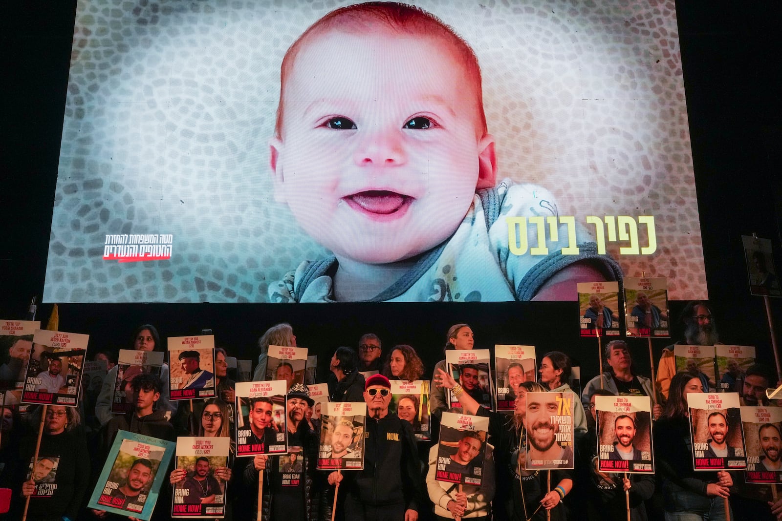 Demonstrators hold portraits of hostages held by Hamas in the Gaza Strip as a video featuring Kfir Bibas, who, along with his parents Shiri and Yarden Bibas, and his brother Ariel, is still being held hostage in Gaza, plays behind them during a protest in Tel Aviv, Israel, Saturday Jan. 18, 2025. (AP Photo/Ohad Zwigenberg, File)