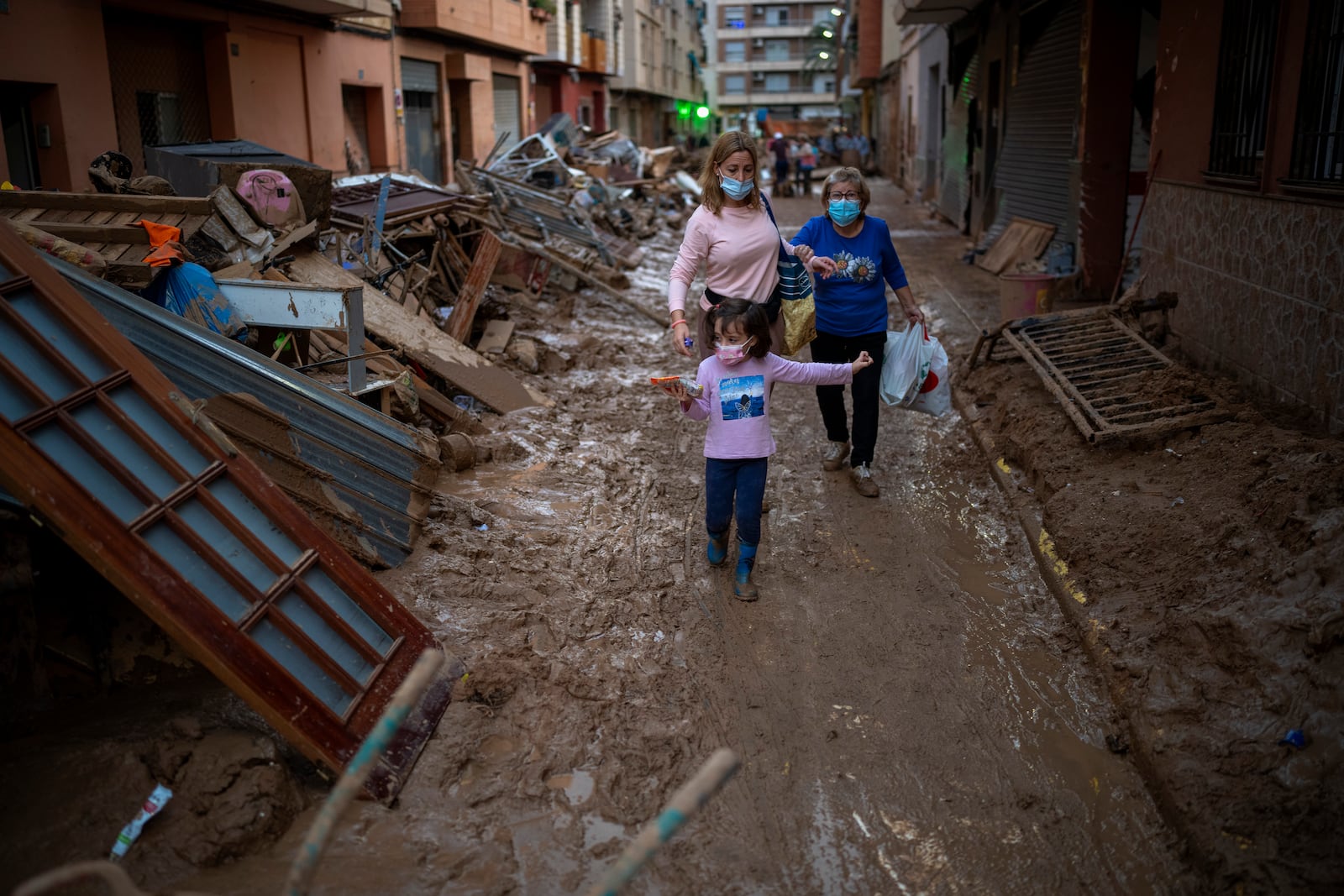 People walk through a street with piled furniture and rubbish on the sides, in an area affected by floods in Paiporta, Valencia, Spain, Tuesday, Nov. 5, 2024. (AP Photo/Emilio Morenatti)