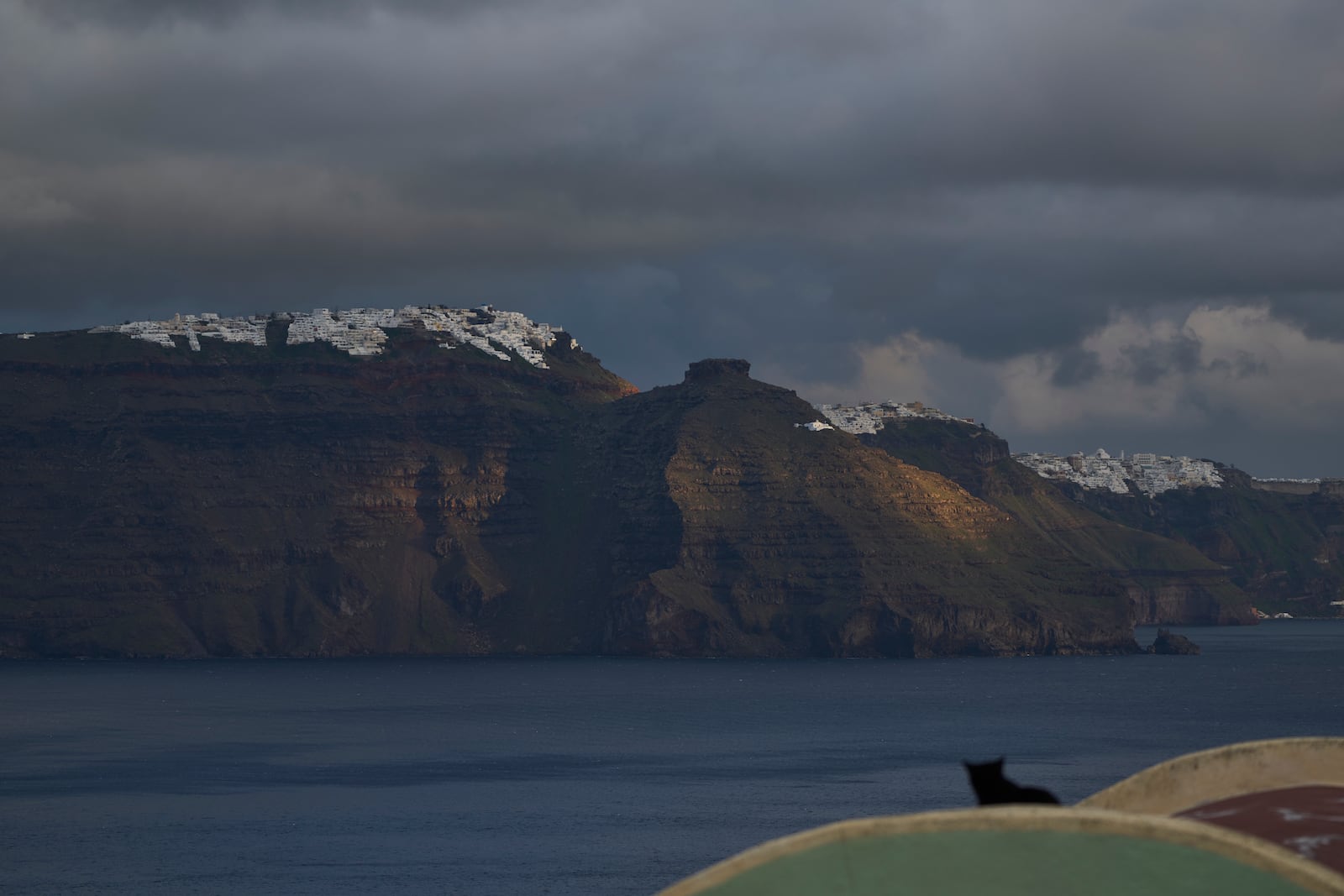 A cat sits on a domed roof in the town of Oia on the earthquake-struck island of Santorini, Greece, as the main town of Fira is seen in the background on Tuesday, Feb. 4, 2025. (AP Photo/Petros Giannakouris)