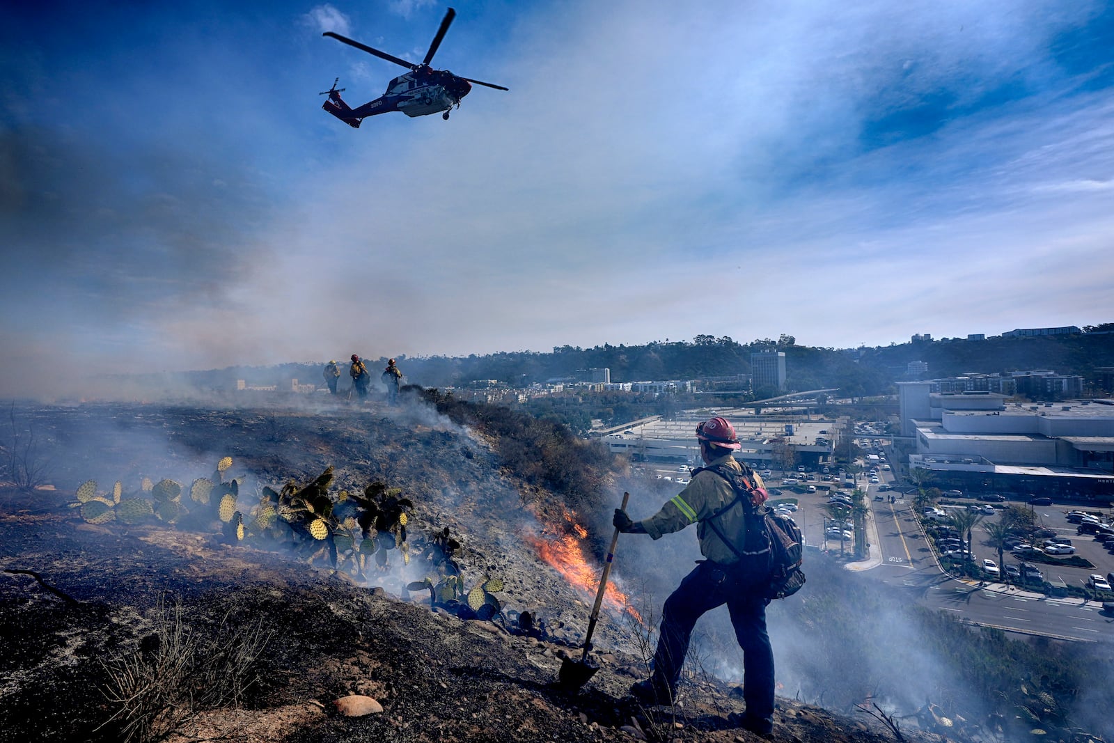 San Diego firefighters knock down a small brush along a hillside over the Mission Valley Shopping Mall in San Diego on Tuesday, Jan. 21, 2025. (AP Photo/Gregory Bull)