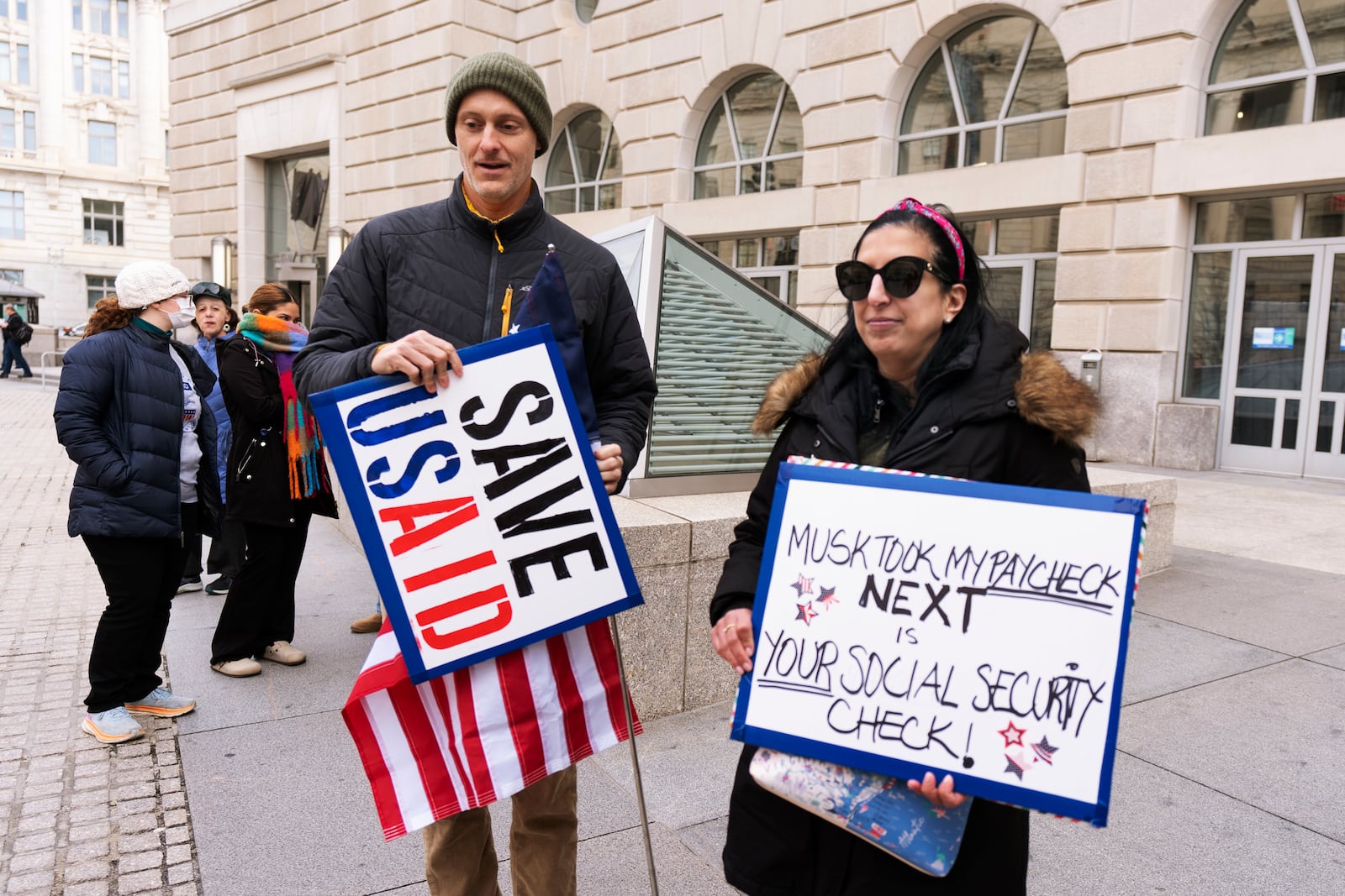 United States Agency for International Development, or USAID contract worker Priya Kathpal, right, and Taylor Williamson, left, who works for a company doing contract work for USAID, carry signs outside the USAID headquarters in Washington, Monday, Feb. 10, 2025. (AP Photo/Manuel Balce Ceneta)