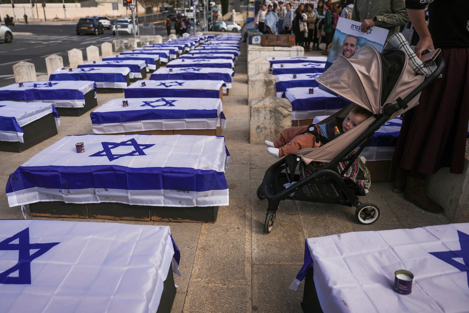 People stand by coffins lining a street and covered with Israeli flags that are meant to symbolize the price Israel will pay for agreeing to a ceasefire with Hamas in a demonstration against the deal staged by a group representing families of Israelis killed during the war in Gaza, in Jerusalem on Thursday, Jan. 16, 2025. (AP Photo/Ohad Zwigenberg)