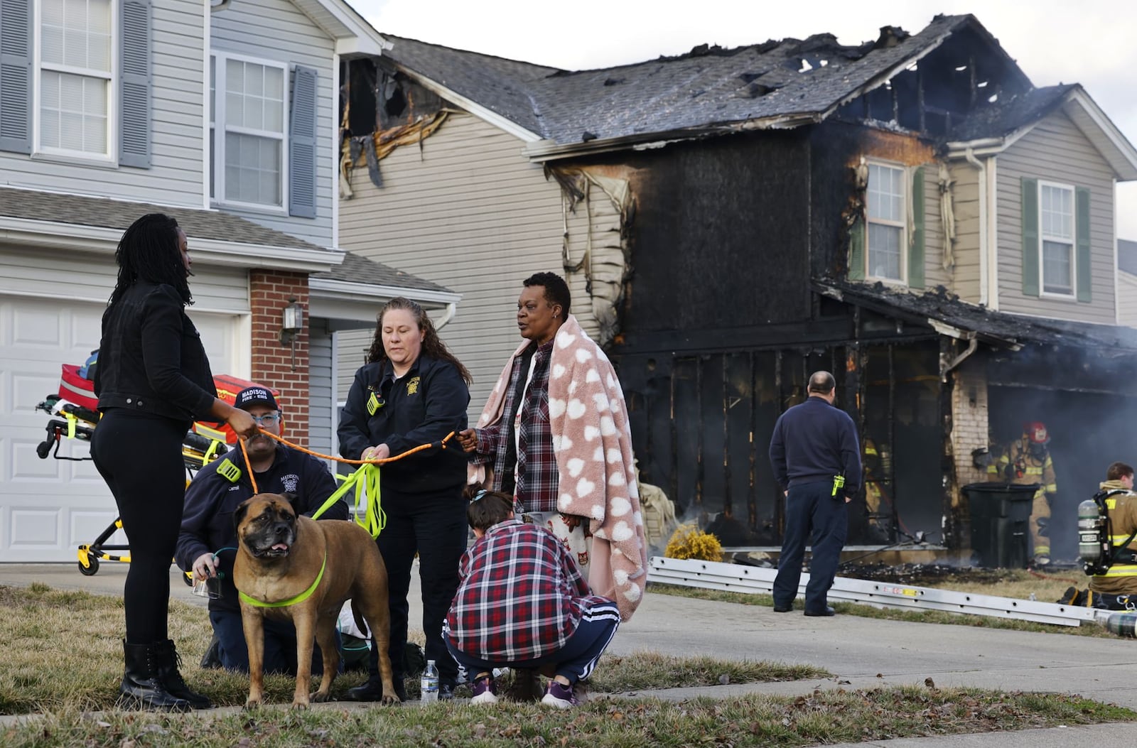 Family dog Apollo is brought to owners Tamela Devereaux, right, and Shanelle Johnson, left, by Madison Twp. Fire Lt. Jessica Shappelle, center, following a fire Friday, Feb. 23, 2024, on Marcia Drive in Trenton. NICK GRAHAM/STAFF