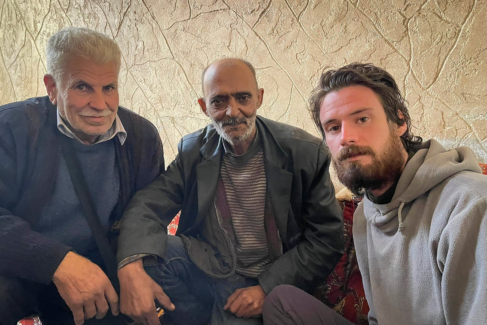 In this photo provided by the Syrian Emergency Task Force, American Travis Timmerman, right, sits with Mosaed al-Rifai, center, who found him in the Syrian desert, and the owner of the house where he took refuge, left, name not available, in Damascus, Syria on Thursday Dec. 12, 2024. (Syrian Emergency Task Force via AP)