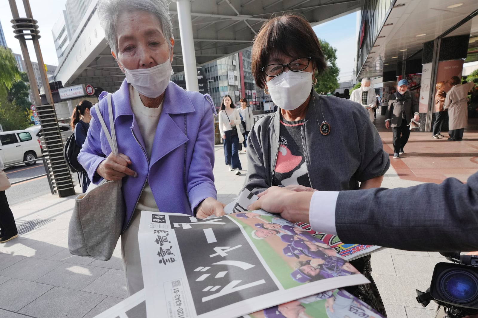 Bystanders receive copies of extra editions of the Yomiuri Shimbun and the Sports Nippon newspapers in Tokyo, Thursday, Oct. 31, 2024, reporting on the Los Angeles Dodgers' victory in the World Series baseball match against the New York Yankees in Game 5 in New York. The headline of the Yomiuri newspaper said "Dodgers is No. 1 in the World." (AP Photo/Eugene Hoshiko)