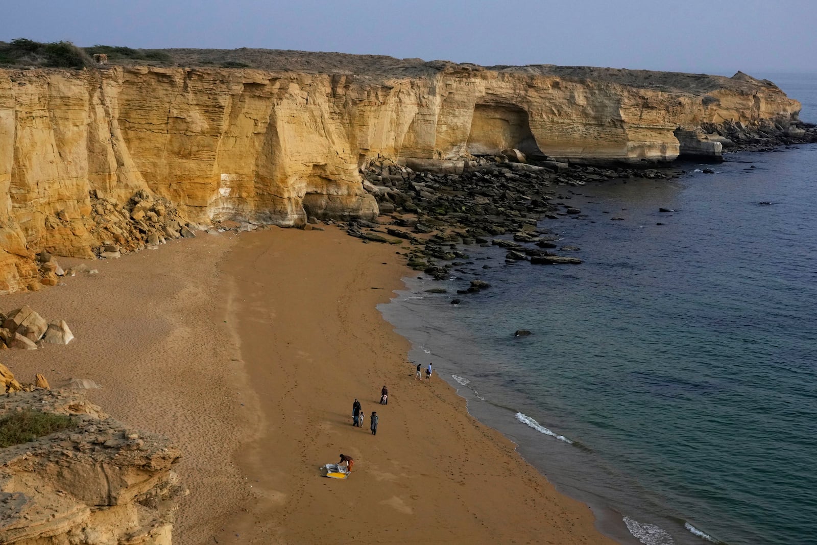 People walk along a beach next to a cliff in Gwadar, Pakistan, Monday, Jan. 13, 2025. (AP Photo/Anjum Naveed)