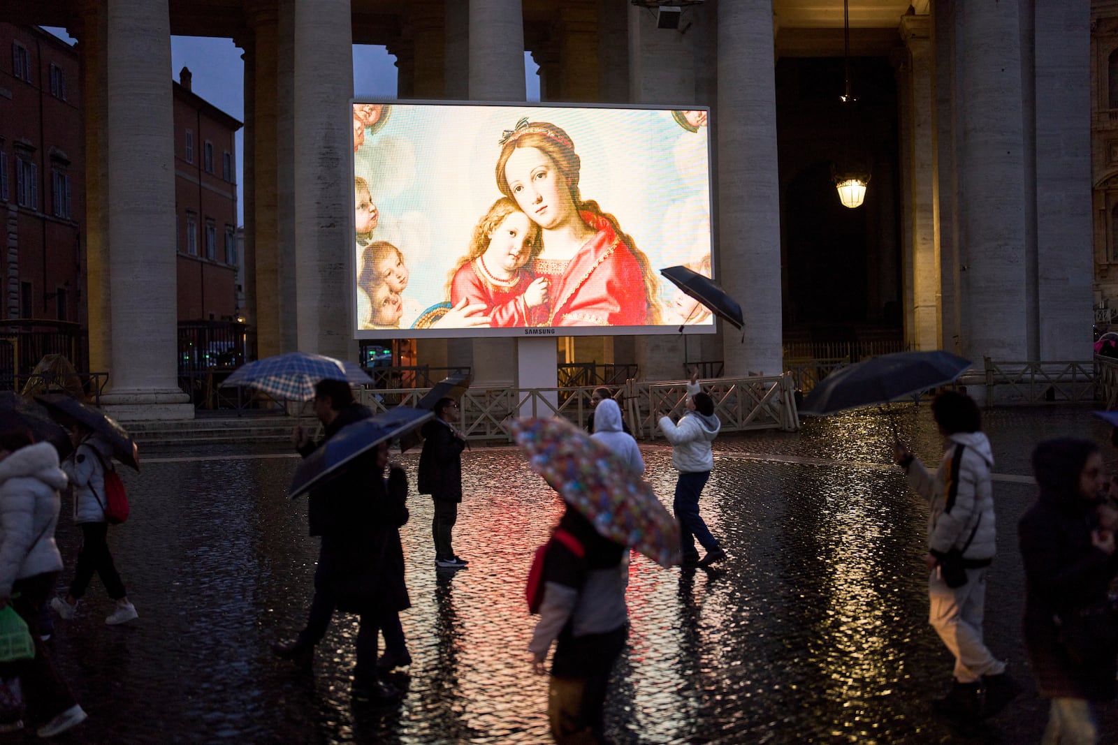 People shelter against the rain as they follow a live broadcasted Rosary prayer for Pope Francis, in St. Peter's Square at the Vatican, Wednesday, March 12, 2025. (AP Photo/Francisco Seco)