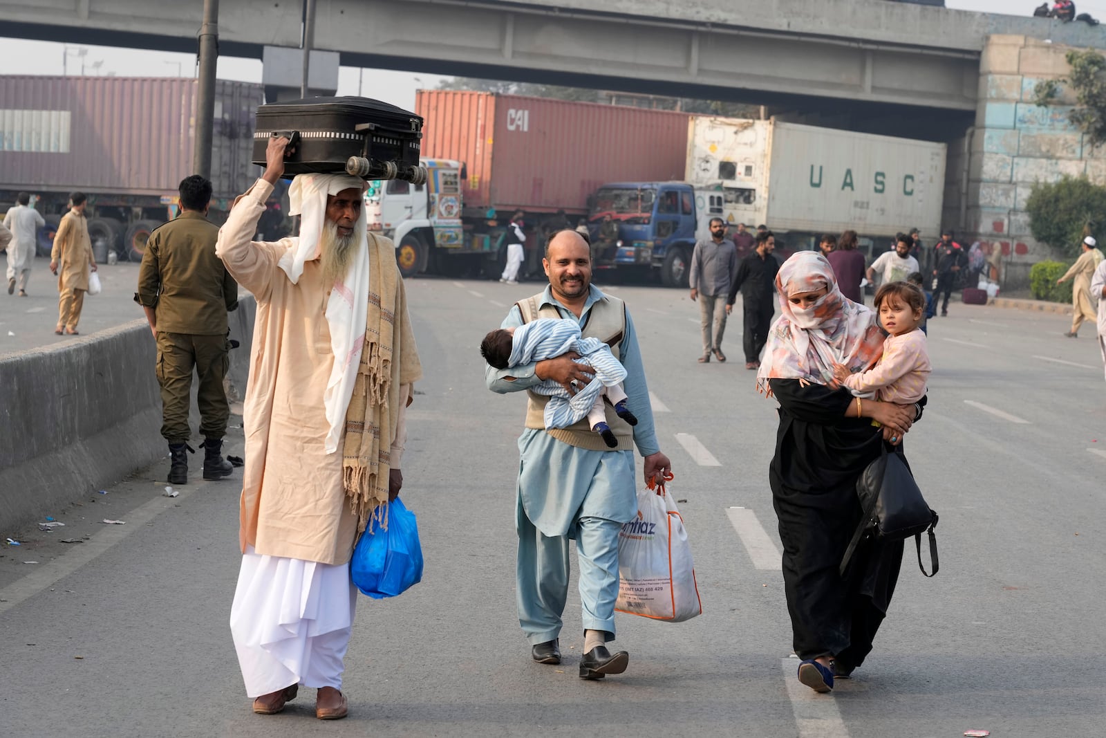 Travellers walk to cross an area barricaded by authorities ahead of a planned rally by supporters of imprisoned former premier Imran Khan's Pakistan Tehreek-e-Insaf party, in Lahore, Pakistan, Sunday, Nov. 24, 2024. (AP Photo/K.M. Chaudary)