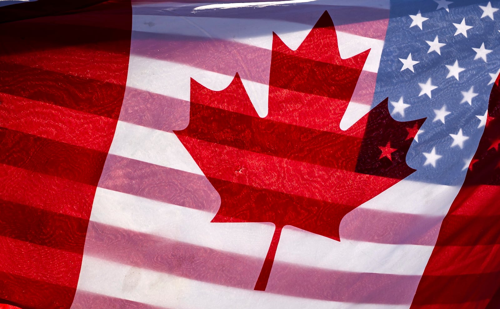 Sunlight shines through the flags of Canada and the United States, held together by a protester outside on Parliament Hill in Ottawa, on Saturday, Feb. 1, 2025.(Justin Tang/The Canadian Press via AP)