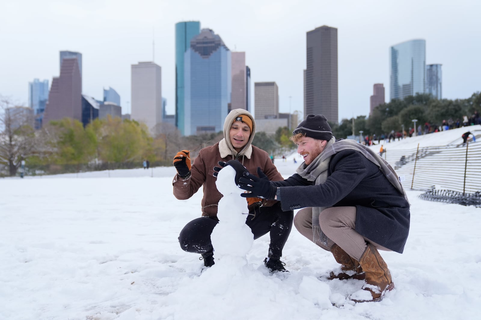 Adrian Santos, left, and Aaron Kenigsberg make a snowman along Buffalo Bayou Tuesday, Jan. 21, 2025, in downtown Houston. (AP Photo/Ashley Landis)