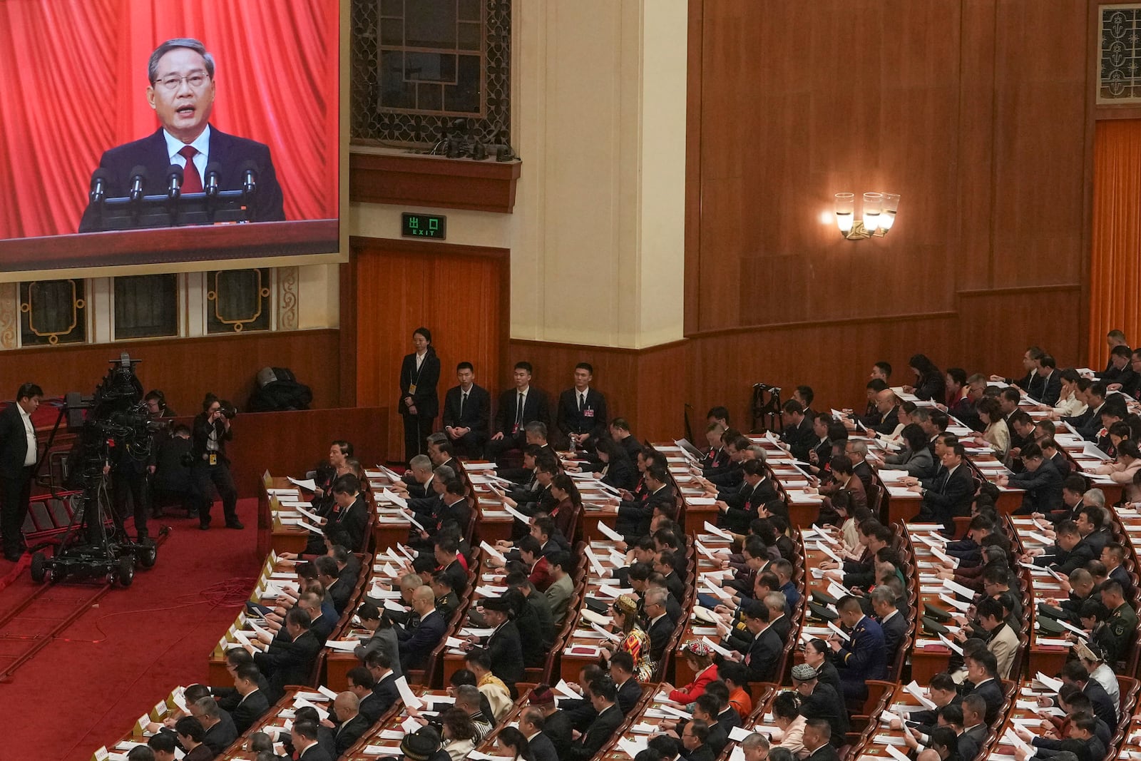 Chinese Premier Li Qiang, on screen, speaks during the opening session of the National People's Congress (NPC) at the Great Hall of the People in Beijing, China, Wednesday, March 5, 2025. (AP Photo/Andy Wong)