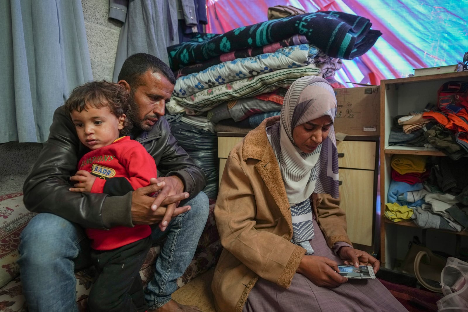 Areej al Qadi, right, shows a picture of one of her three dead children as her husband Mahmoud bin Hassan, left, holds a fourth surviving child at their tent in a refugee camp in Deir al-Balah, Gaza Strip, Thursday Nov. 21, 2024. Seven-year-old Hamza, his five-year-old brother Abdelaziz, and his four-year-old sister Laila Hassan were among 9 people killed by an Israeli strike in Khan Younis on Wednesday. Palestinian health officials say the death toll in the Gaza Strip from the 13-month-old war between Israel and Hamas has surpassed 44,000. (AP Photo/Abdel Kareem Hana)