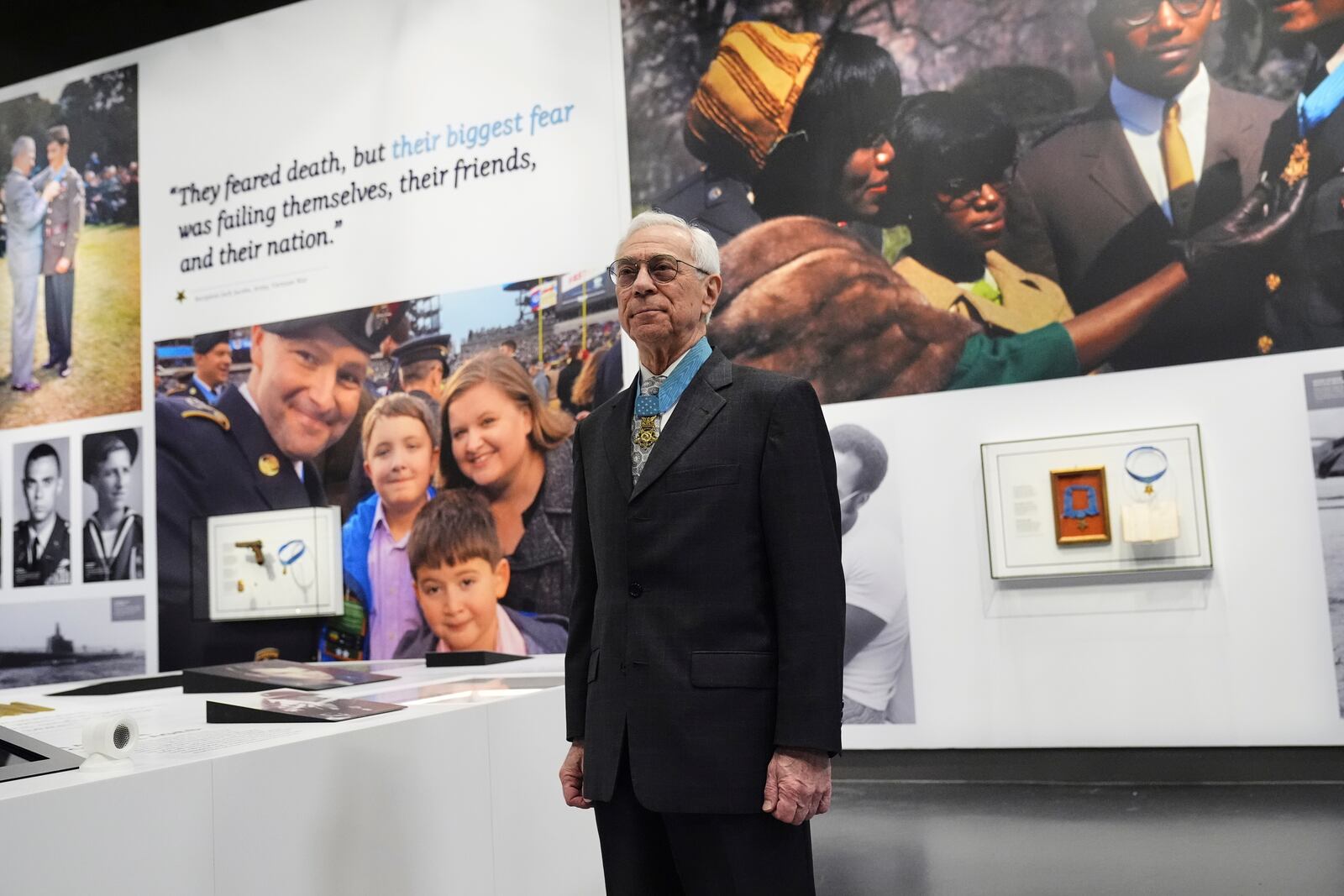 Jack Jacobs, a retired U.S. Army colonel who was awarded the Medal of Honor for his actions during the Vietnam War, poses for a photo in front of one of his quotes, seen on the top left rear of the wall, on display at the National Medal of Honor Museum in Arlington, Texas, Thursday, March 13, 2025. (AP Photo/Tony Gutierrez)