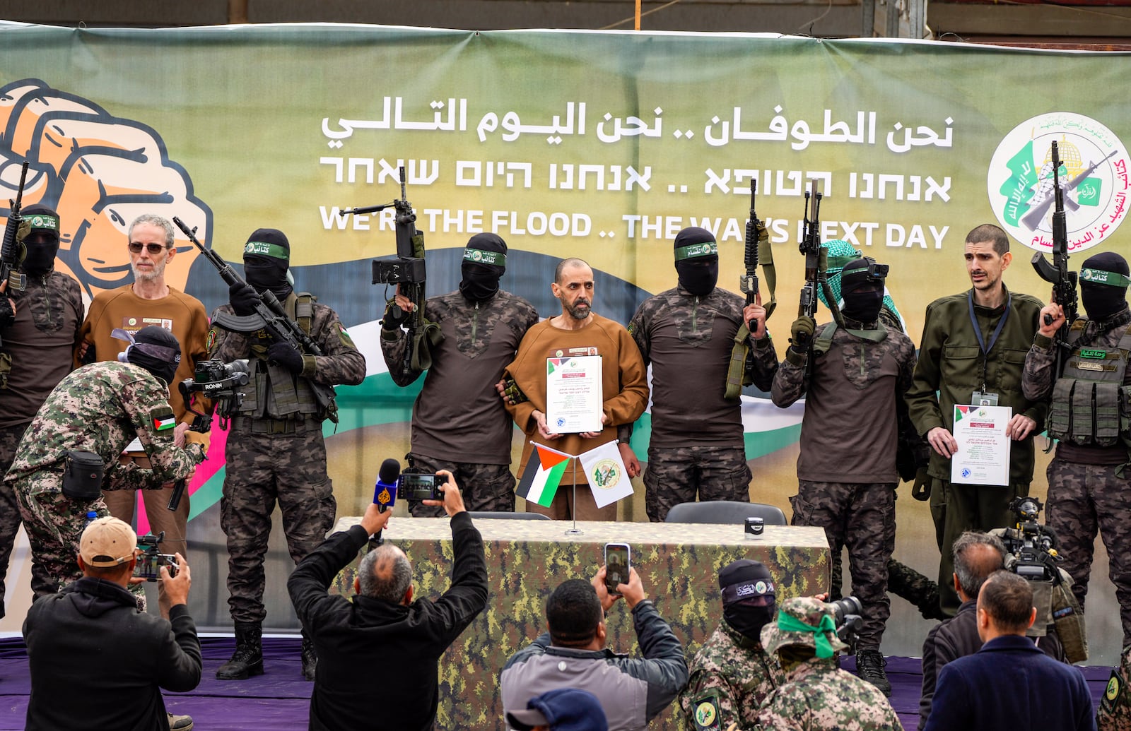 Israeli captives, from left to the right, Ohad Ben Ami, Eli Sharabi and Or Levy, who have been held hostage by Hamas in Gaza since October 7, 2023, satnd escorted by Hamas fighters on a stage before being handed over to the Red Cross in Deir al-Balah, central Gaza Strip, Saturday Feb. 8, 2025. (AP Photo/Abdel Kareem Hana)