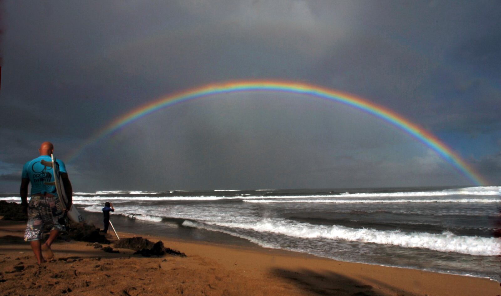 FILE - Professional surfers make their way to the water while a large rainbow crosses the ocean during the Pro Hawaii surfing contest at Ali'i Beach in Haleiwa, Hawaii, Nov. 18, 2005. (AP Photo/Lucy Pemoni, File)