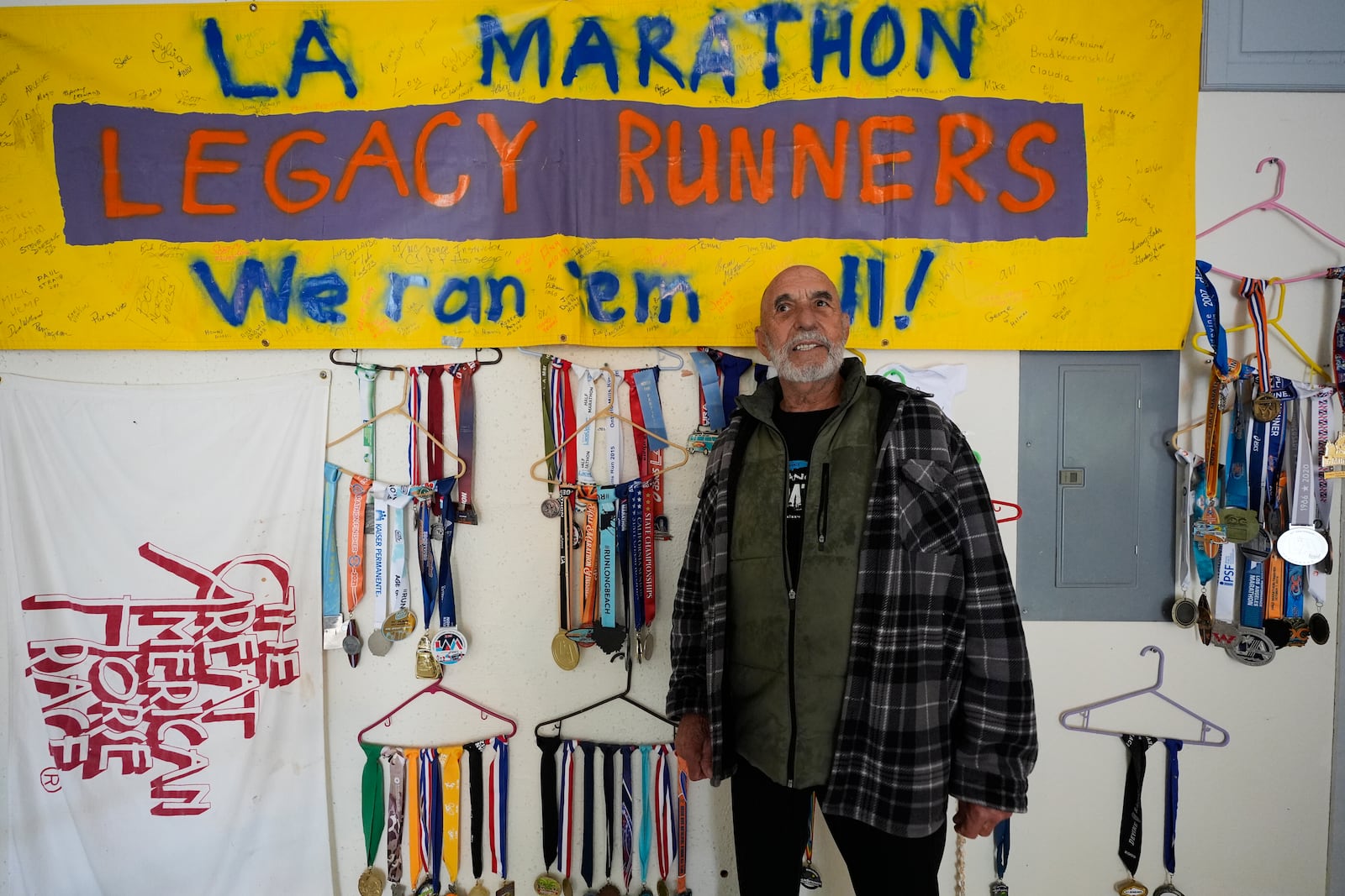 Rick Bingham, 87, currently training for the Los Angeles Marathon, poses for a photo next to some of his competition medals at home in Lake Elsinore, Calif., Tuesday, March 11, 2025. (AP Photo/Damian Dovarganes)