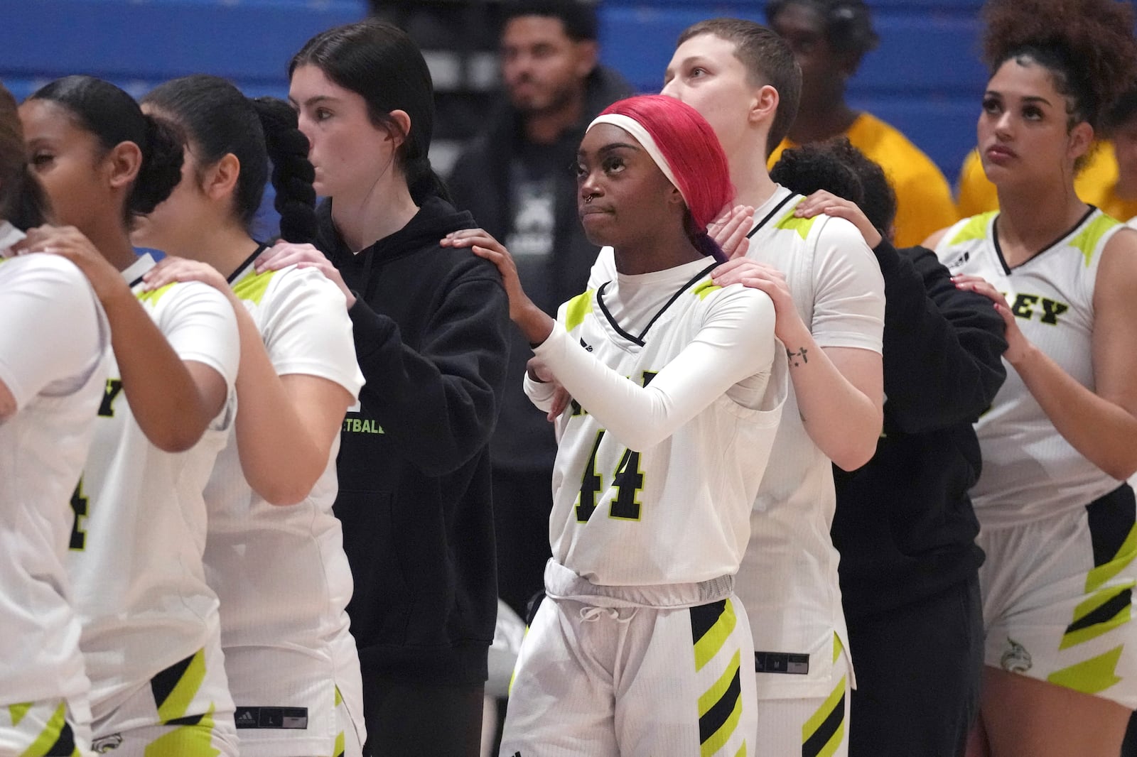 Lesley College basketball player Baileigh Sinaman-Daniel, center, joins teammates for the national anthem prior to a game against Vermont State Lyndon, Tuesday, Feb. 11, 2025, in Lexington, Mass. (AP Photo/Charles Krupa)