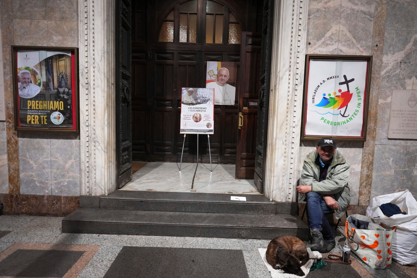 A man sits with his dog outside the Church of the Argentinas before the Pope's Vicar for Rome, Cardinal Baldassare Reina celebrates mass for the health of Pope Francis, Santa Maria Addolorata in Rome, Italy Tuesday, Feb. 25, 2025. (AP Photo/Kirsty Wigglesworth)