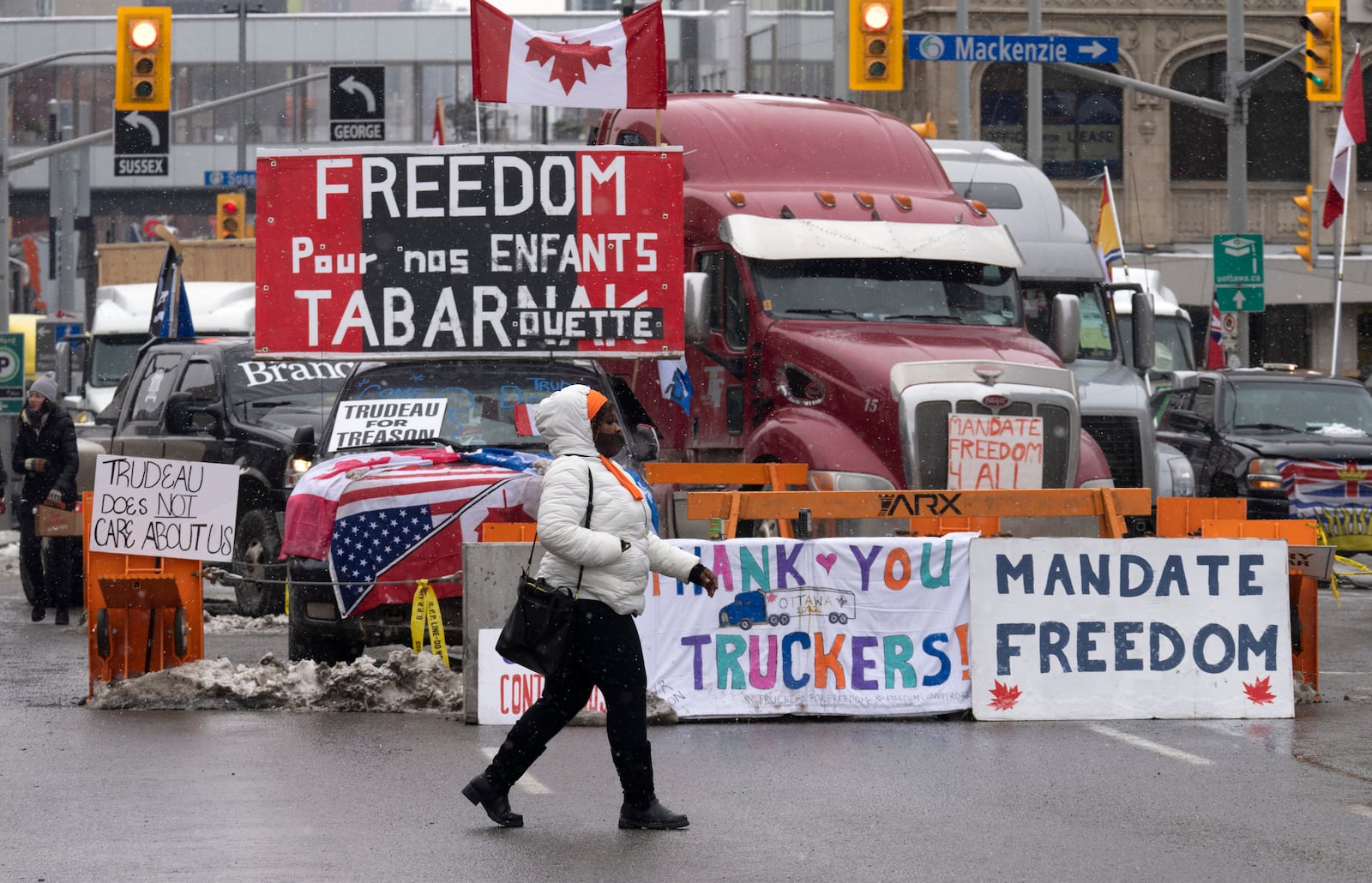 FILE - A woman crosses the street in front of vehicles parked as part of the trucker protest, on Feb. 8, 2022 in Ottawa. Canadian lawmakers expressed increasing worry about protests over vaccine mandates other other COVID restrictions after the busiest border crossing between the U.S. and Canada became partially blocked. (Adrian Wyld /The Canadian Press via AP, File)