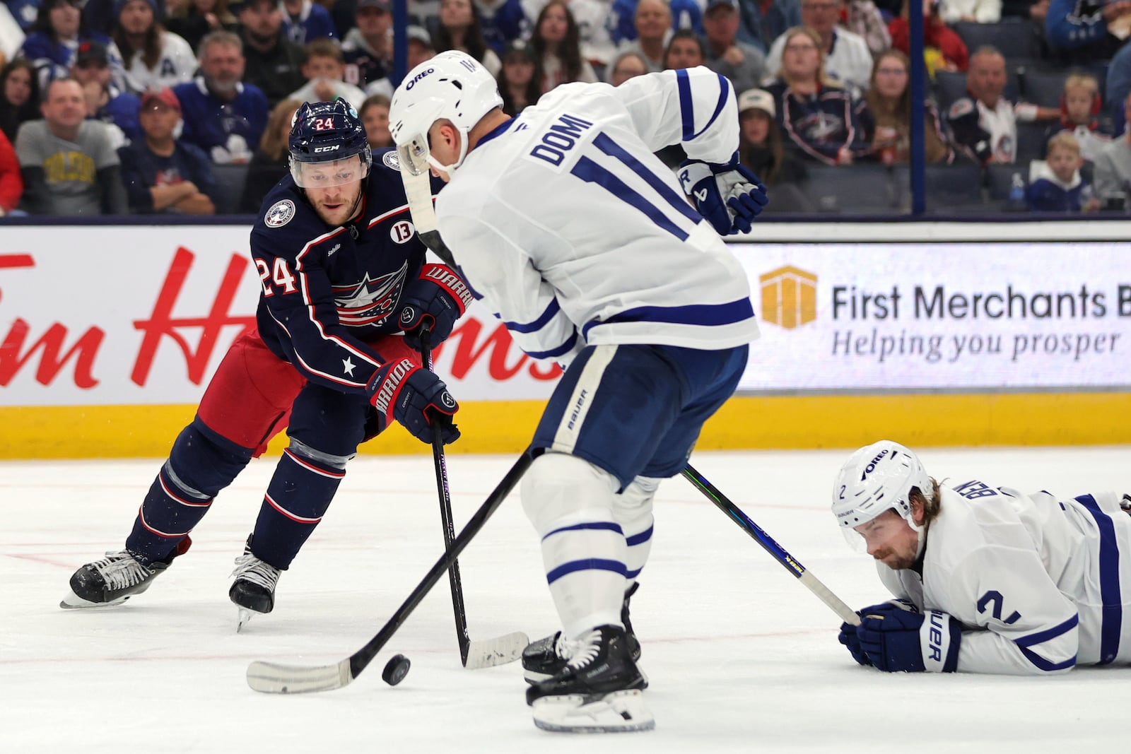 Columbus Blue Jackets forward Mathieu Olivier, left, reaches for the puck in front of Toronto Maple Leafs forward Max Domi, center, and forward Simon Benoit during the second period of an NHL hockey game in Columbus, Ohio, Tuesday, Oct. 22, 2024. (AP Photo/Paul Vernon)