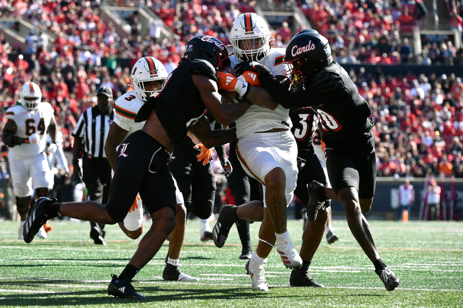 Louisville defensive back Benjamin Perry (10), left, and defensive back Tayon Holloway (20) right, try to bring down Miami running back Damien Martinez (6) during the second half of an NCAA college football game in Louisville, Ky., Saturday, Oct. 19, 2024. Miami won 52-45. (AP Photo/Timothy D. Easley)