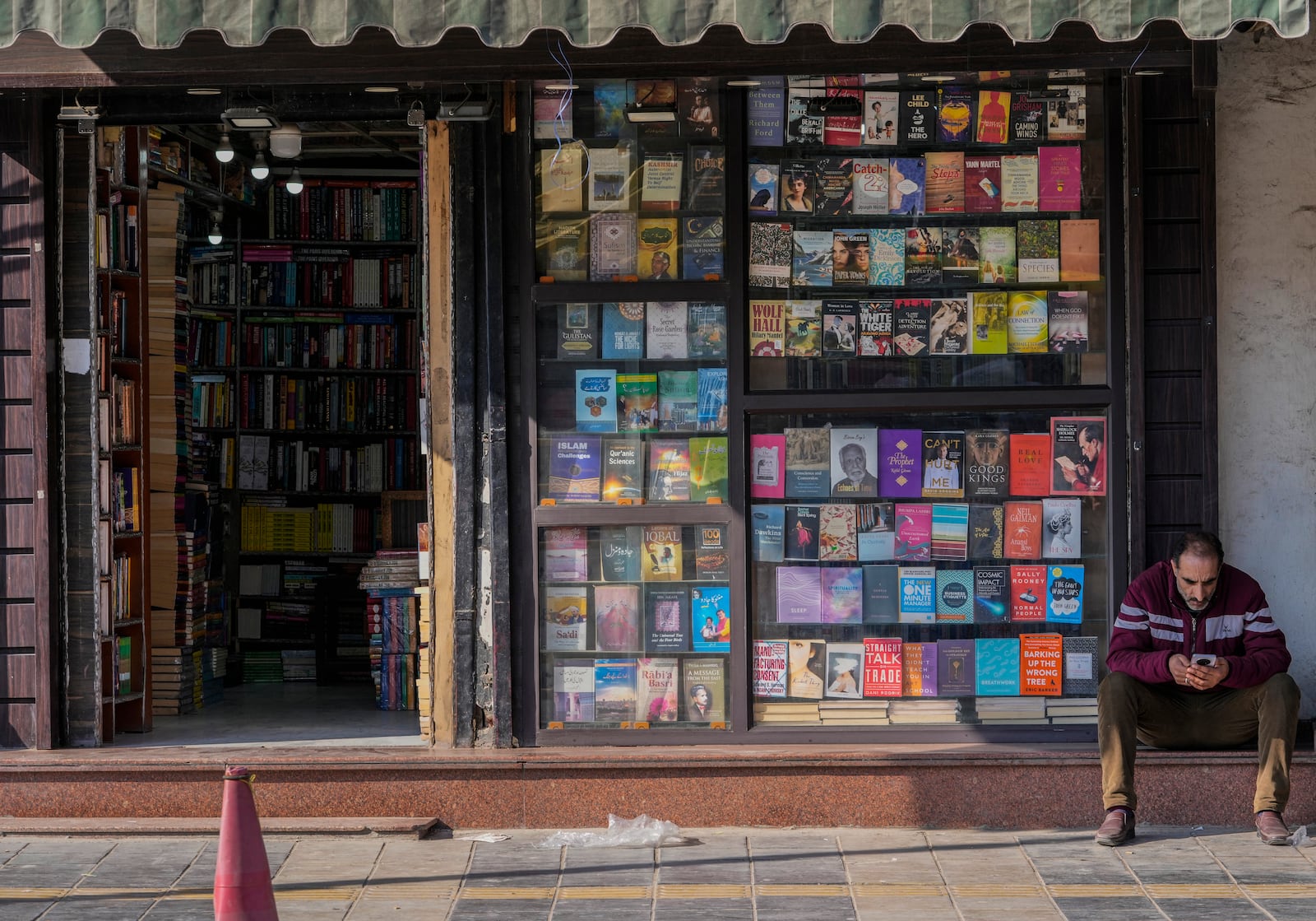 A man checks his cell phone as he rests outside a book shop in Srinagar, Indian controlled Kashmir, Monday, Feb. 17, 2025. (AP Photo/Mukhtar Khan)