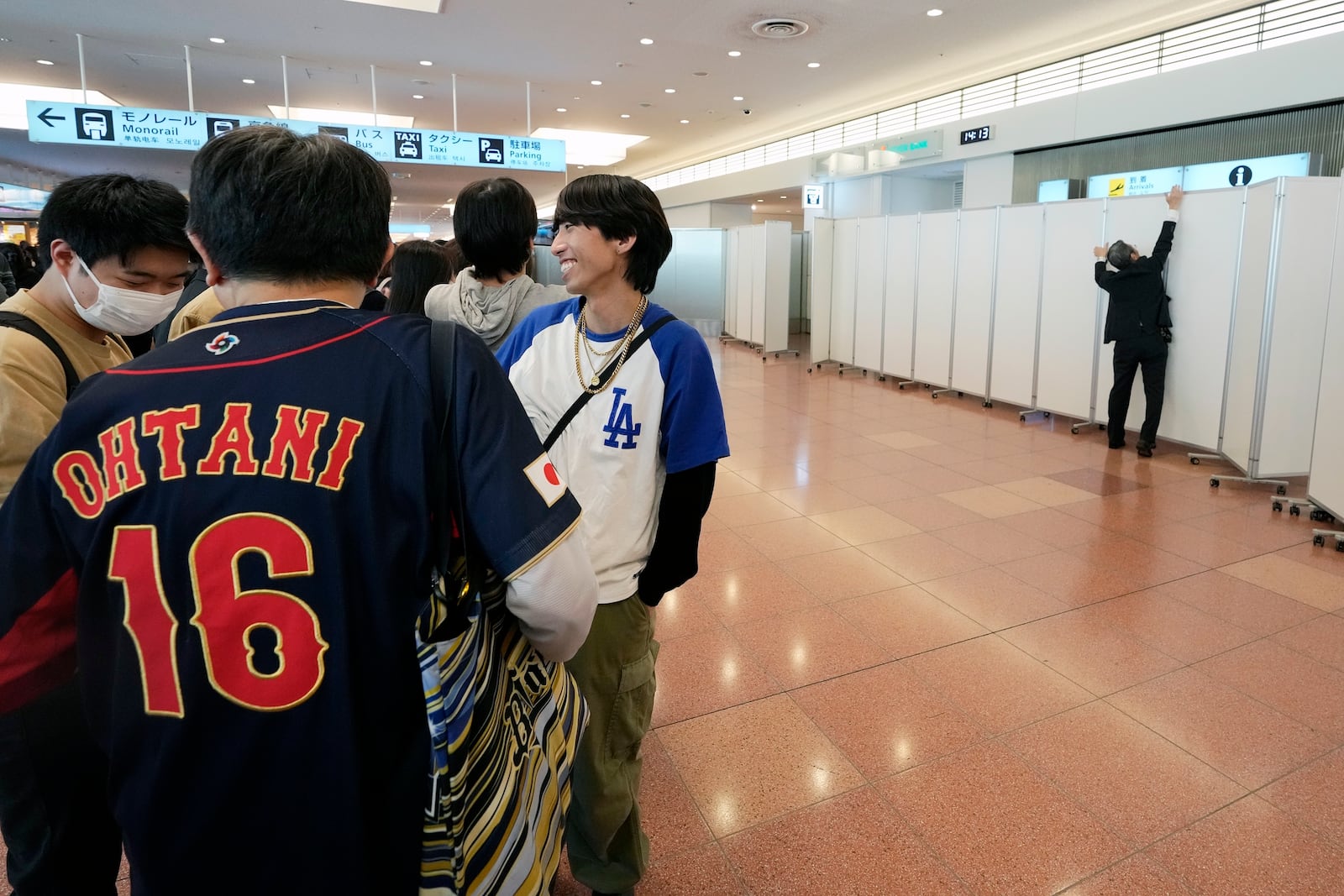 Fans of Los Angeles Dodgers wait for the team arrival as a staff installs partitions to block fans from the arrival route of the Dodgers team members at Tokyo International Airport Thursday, March 13, 2025, in Tokyo, as Dodgers to play their MLB opening games against and Chicago Cubs in Tokyo on March 18-19. (AP Photo/Hiro Komae)