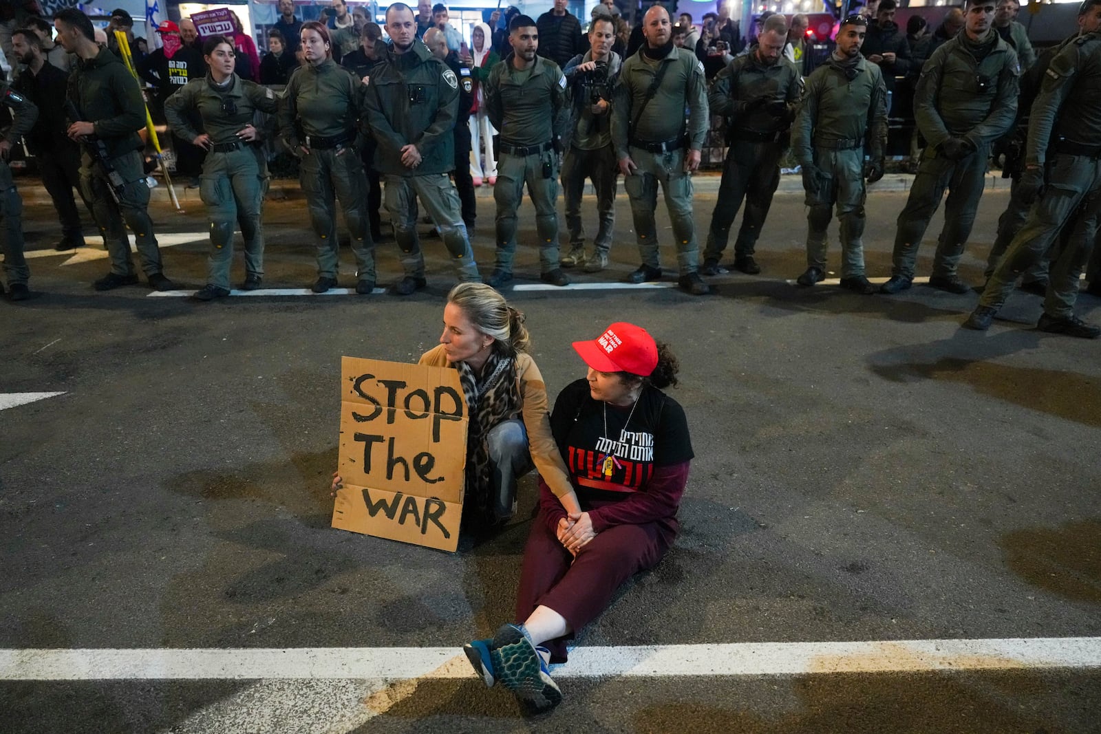 Demonstrators sit on the road and hold a sign during a protest demanding a cease-fire deal and the immediate release of hostages held in the Gaza Strip by Hamas, in Tel Aviv, Israel, Saturday, Jan. 11, 2025. (AP Photo/Ariel Schalit)