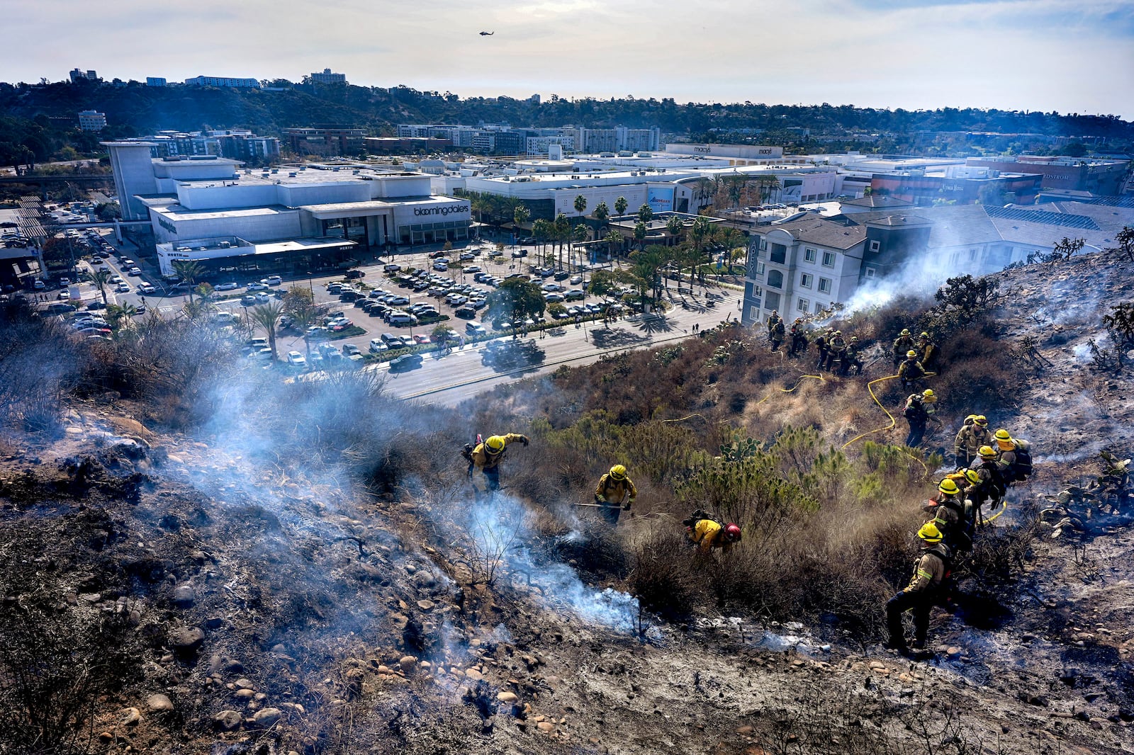 San Diego firefighters knock down a small brush along a hillside over the Mission Valley Shopping Mall in San Diego on Tuesday, Jan. 21, 2025. (AP Photo/Gregory Bull)