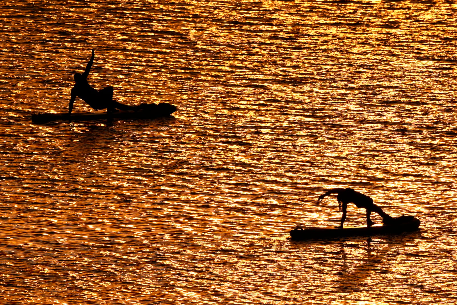 FILE - People do yoga poses on paddleboards at sunset at Olathe Lake on July 15, 2024, in Olathe, Kan. (AP Photo/Charlie Riedel, File)