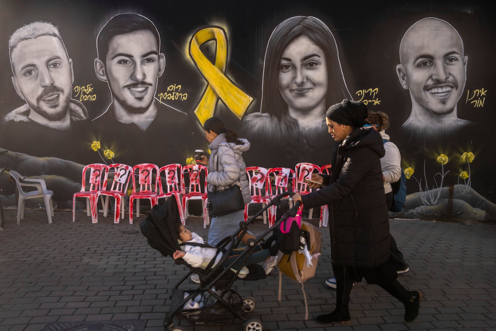 An ultra-Orthodox Jewish woman walks past an installation, and a mural of portraits of hostages held by Hamas, in Gaza, in Jerusalem, Tuesday, Jan. 21, 2025. (AP Photo/Ohad Zwigenberg)