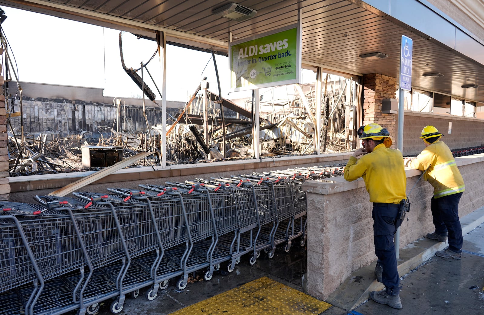 Clean-up workers look inside the interior of Aldi Food Market after it was destroyed by the Eaton Fire, Sunday, Jan. 12, 2025, in Altadena, Calif. (AP Photo/Chris Pizzello)