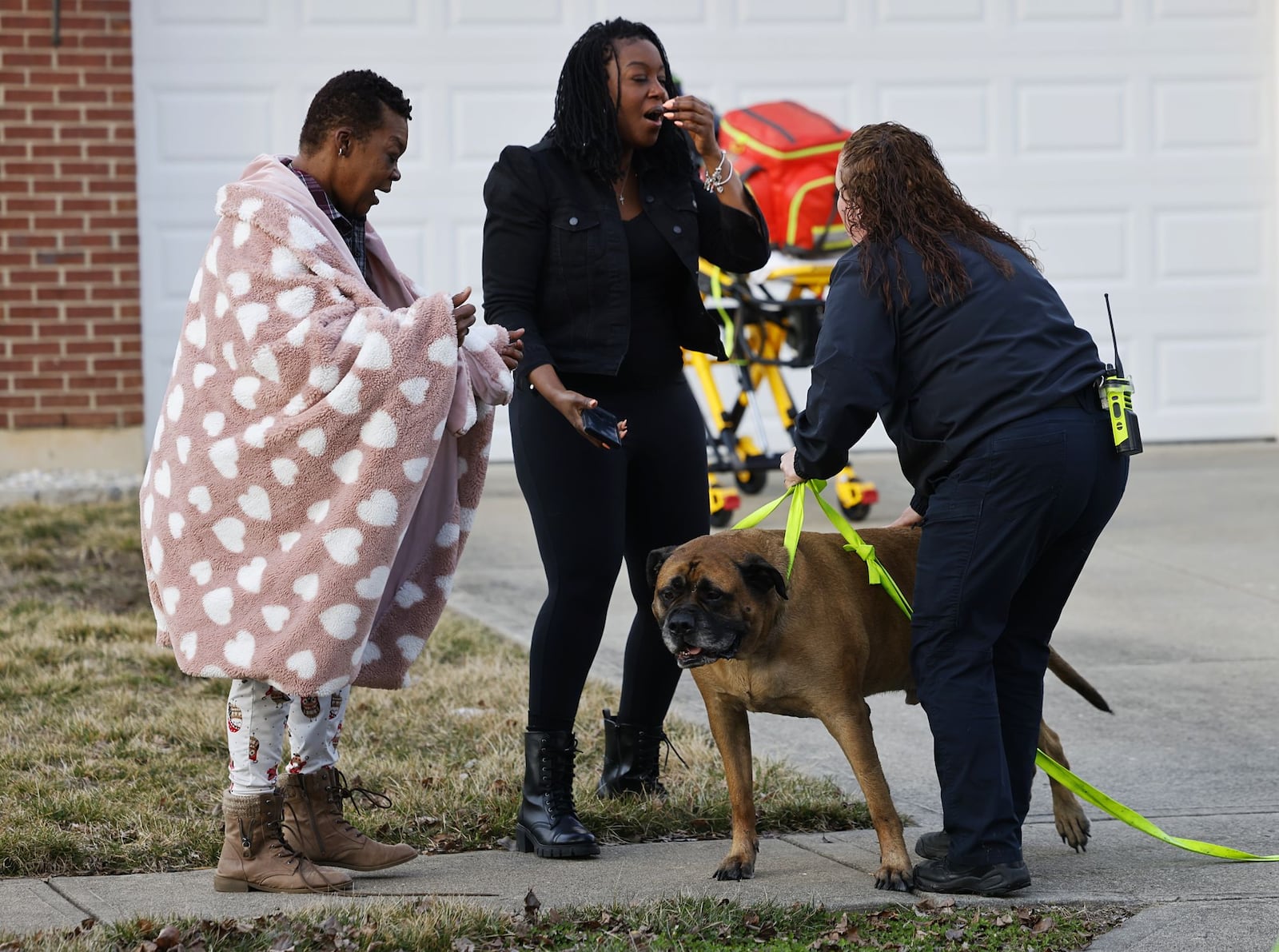 Apollo is reunited with his owners Tamela Devereaux, left, and Shanelle Johnson, center, by Madison Twp. Fire Lt. Jessica Shappelle, right, after he was rescued from a house fire Friday, Feb. 23, 2024, on Marcia Drive in Trenton. NICK GRAHAM/STAFF